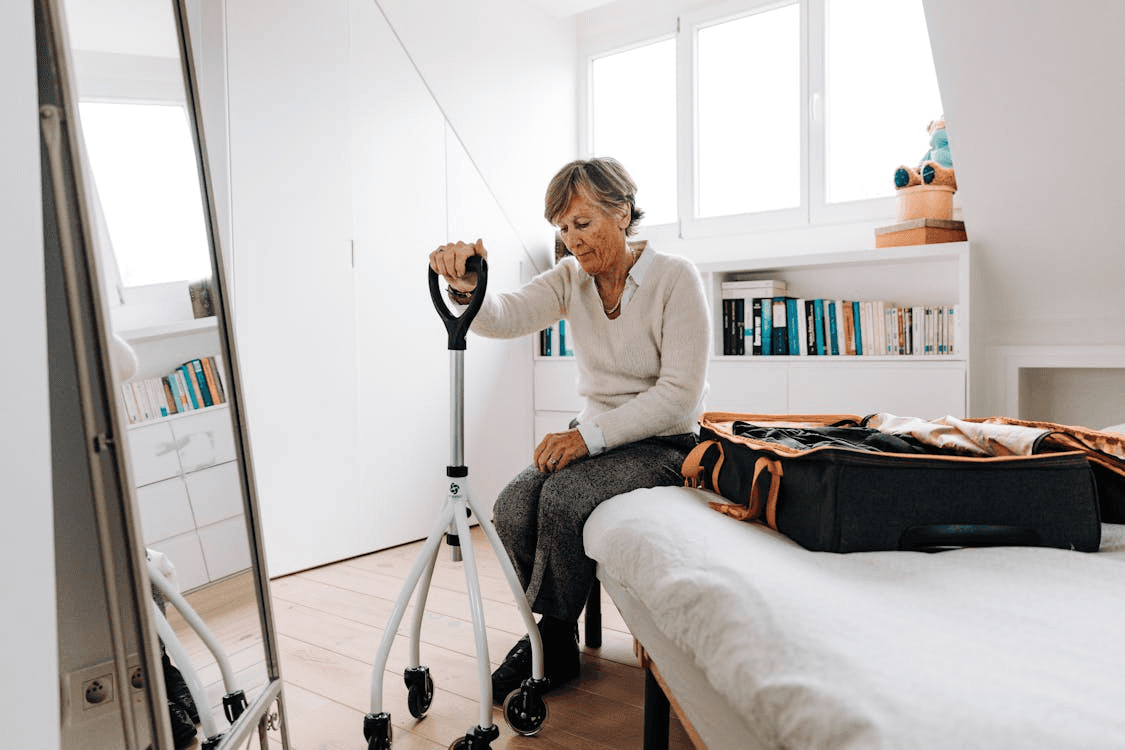 An aged care resident sitting on their bed as they hold onto their walking stick to help prevent falls that can lead to life threatening injury.