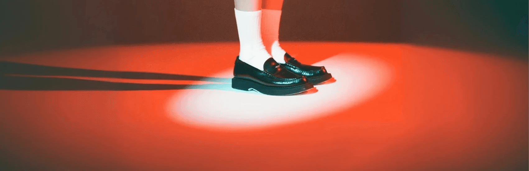 Close-up of black leather loafers worn with white socks, lit by red and blue lighting.