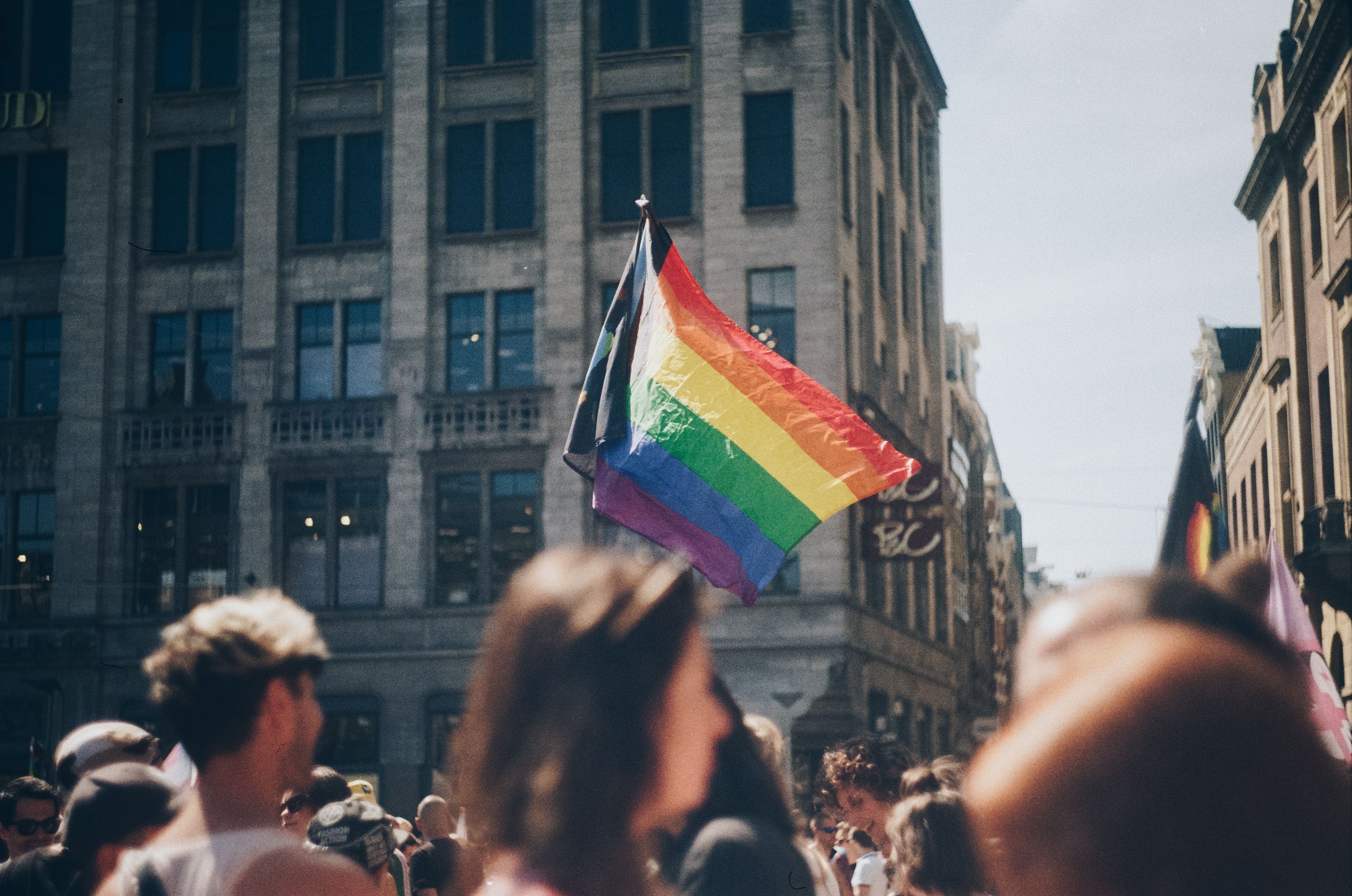 a picture of a rainbow pride flag in the middle of a crowded street during a march.