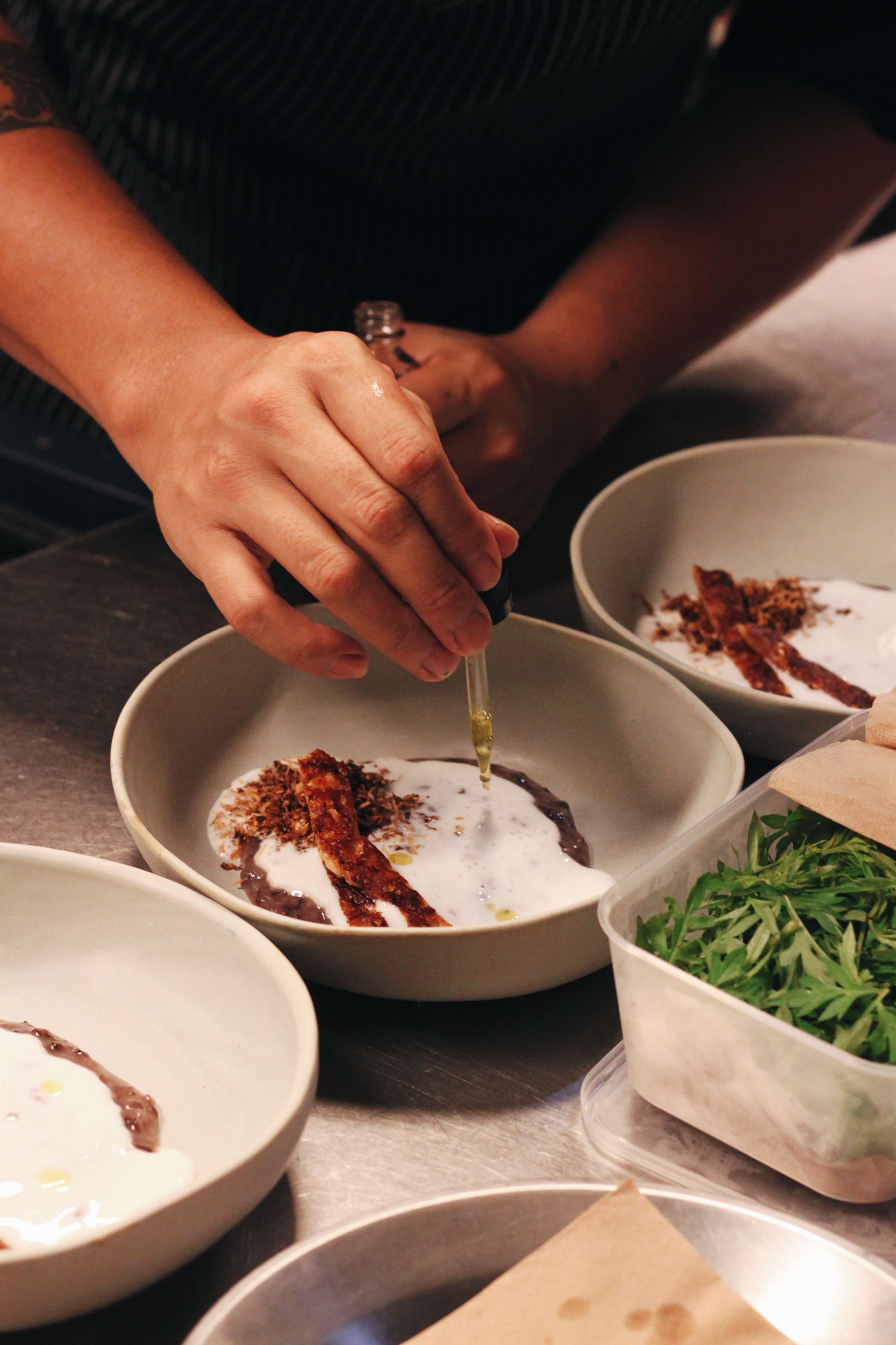 Chef plating a dish with a pipette in a professional kitchen