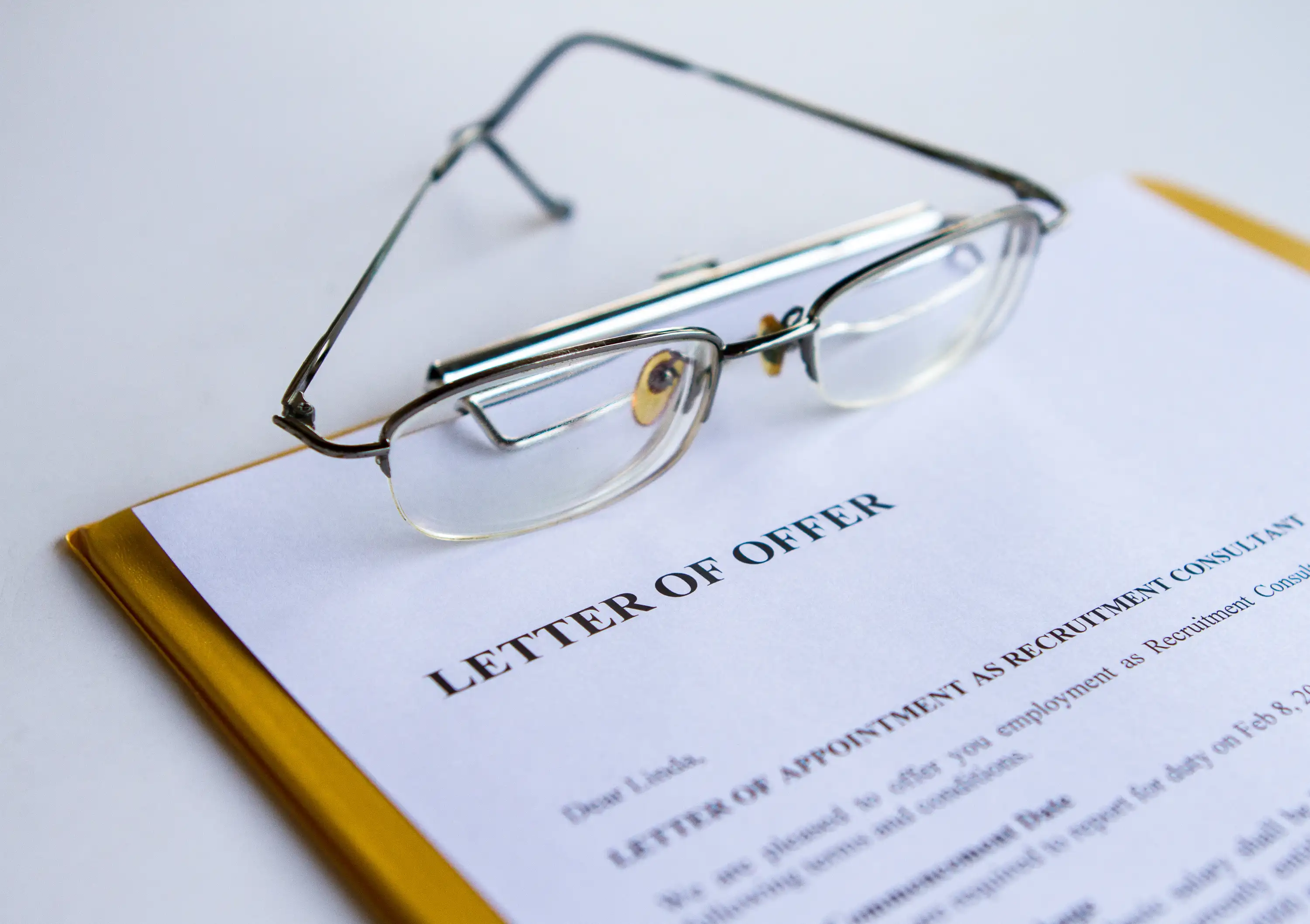 Eyeglasses resting on an employment offer letter, illustrating at-will contract reviews in California job relocation fraud cases under Labor Code 970