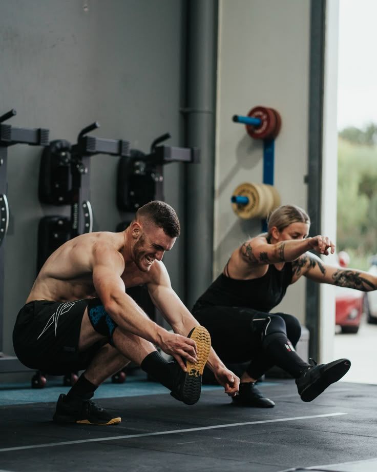Two people performing single-leg squats in a gym.