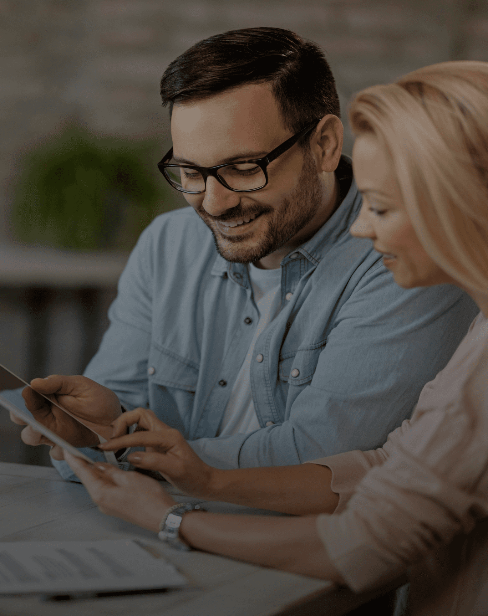 A man and a woman smile while looking at a tablet, engaged in conversation. They appear focused and collaborative.