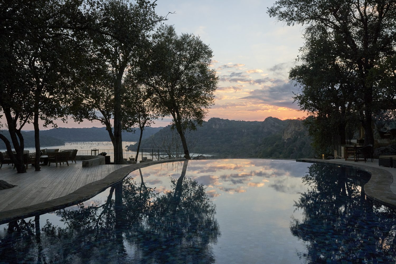 The infinity pool at Singita Pamushana at dusk, the Malilangwe lake and sandstone hills beyond