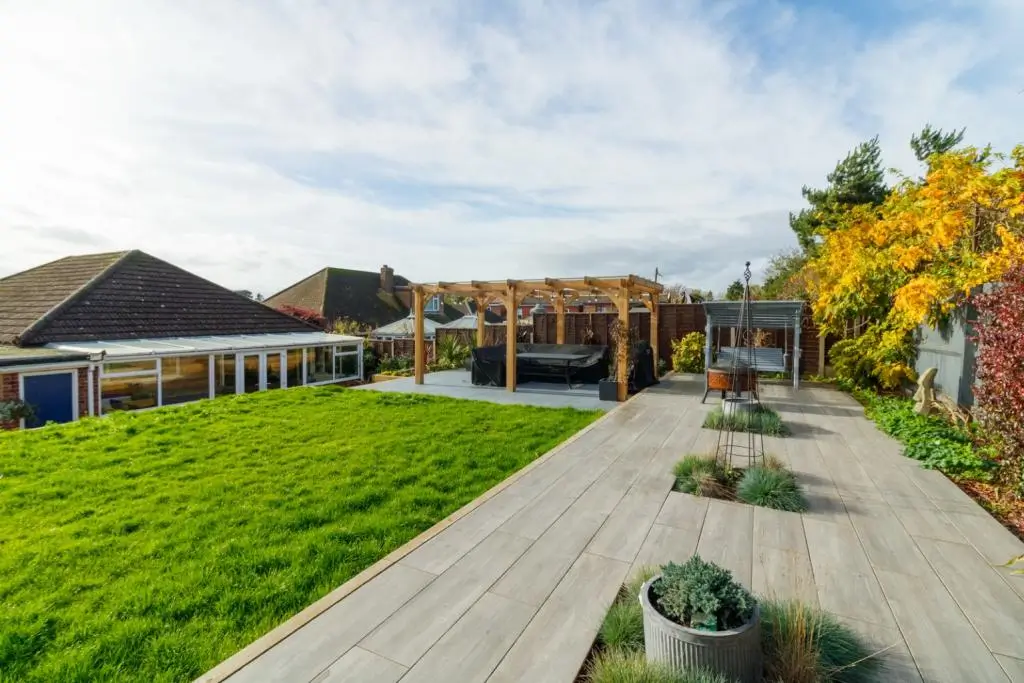 A landscaped garden featuring a pathway, green grass, trees, and a clear blue sky in the background.