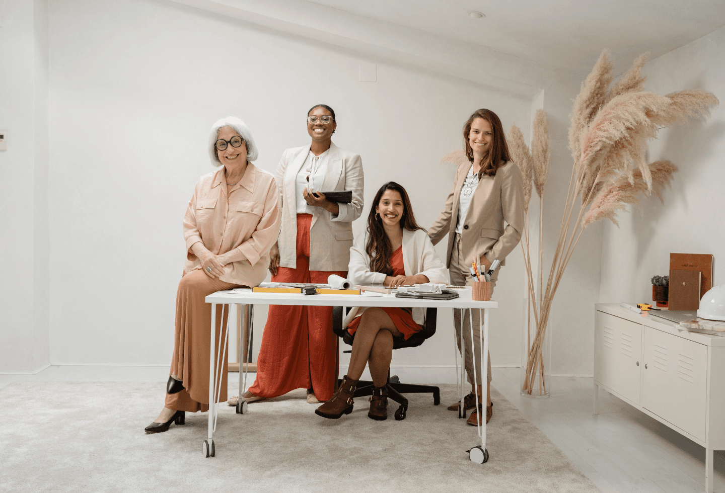A diverse team of four women architects smiling together in a bright, modern office.
