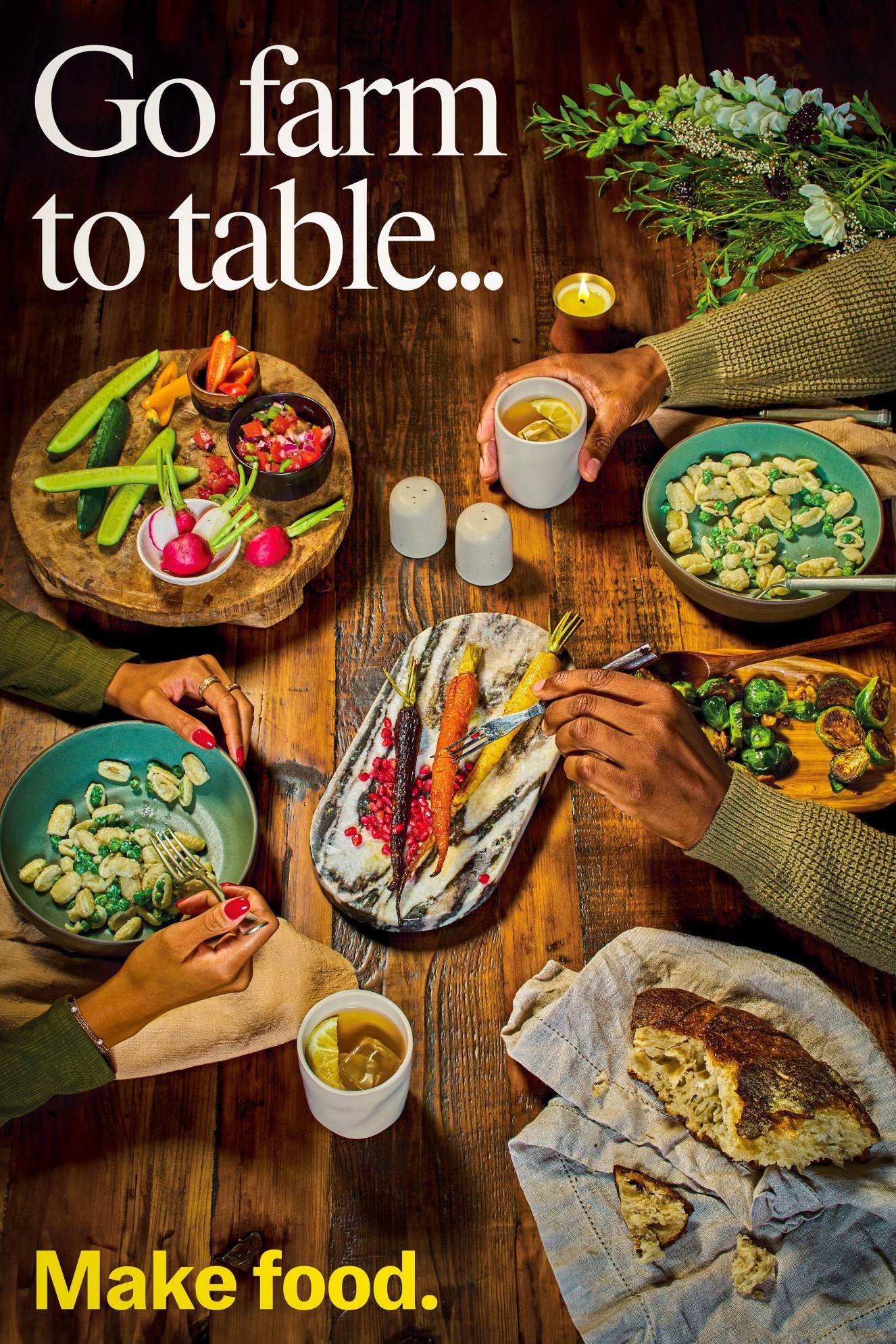 Overhead farm to table dinner with vegetables, bread, pasta, tea, flowers, and two diners at a wooden table