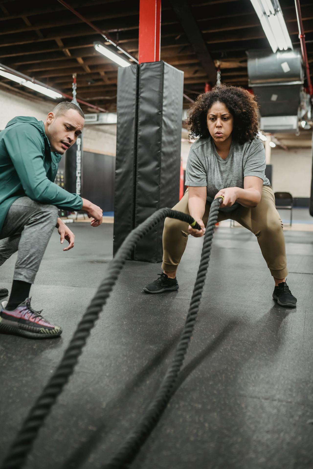 Concentrated black woman exercising with battle ropes in contemporary gym