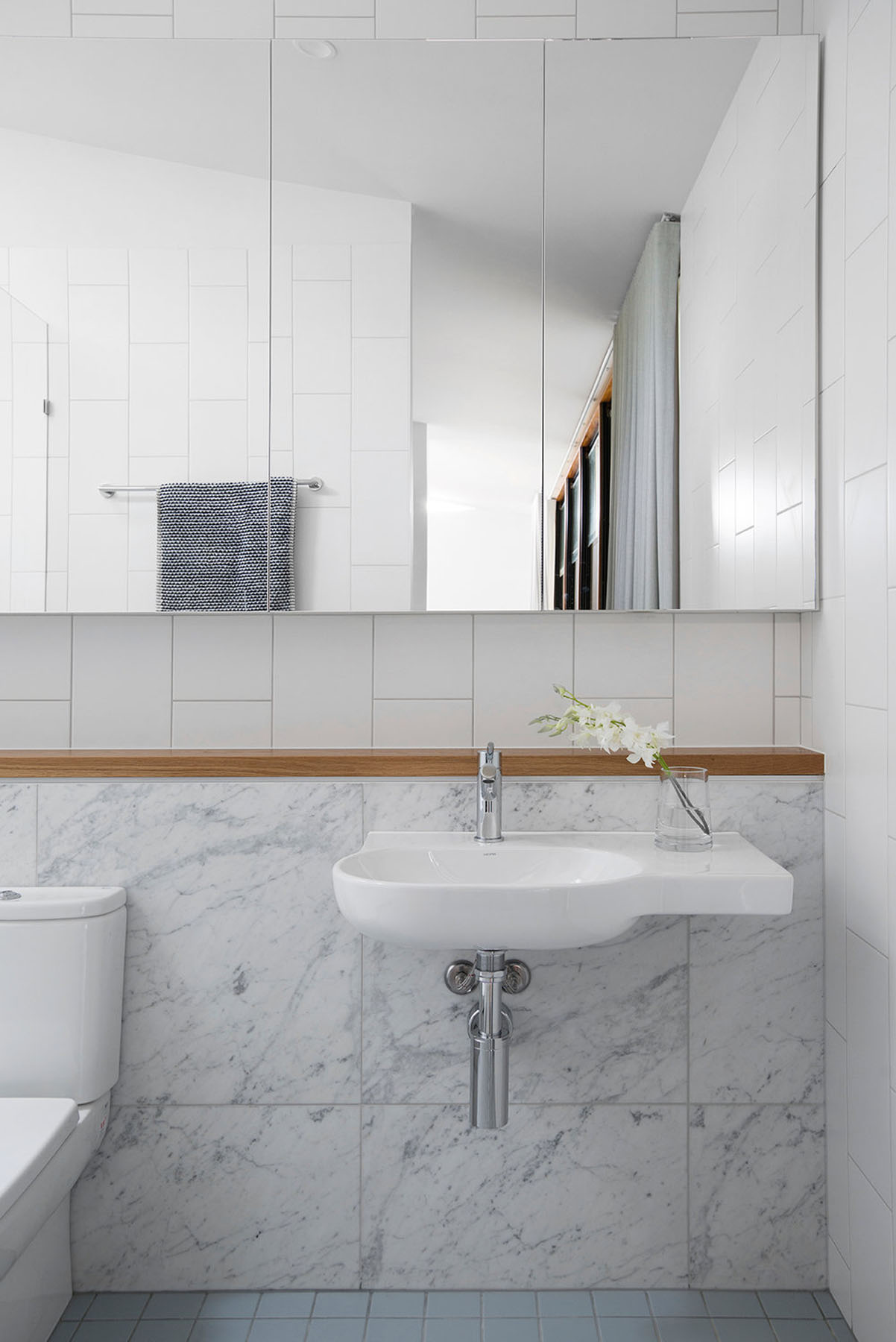 Linear ensuite with marble finishes, wall-mounted basin, and full-height glazing drawing light deep into the plan.