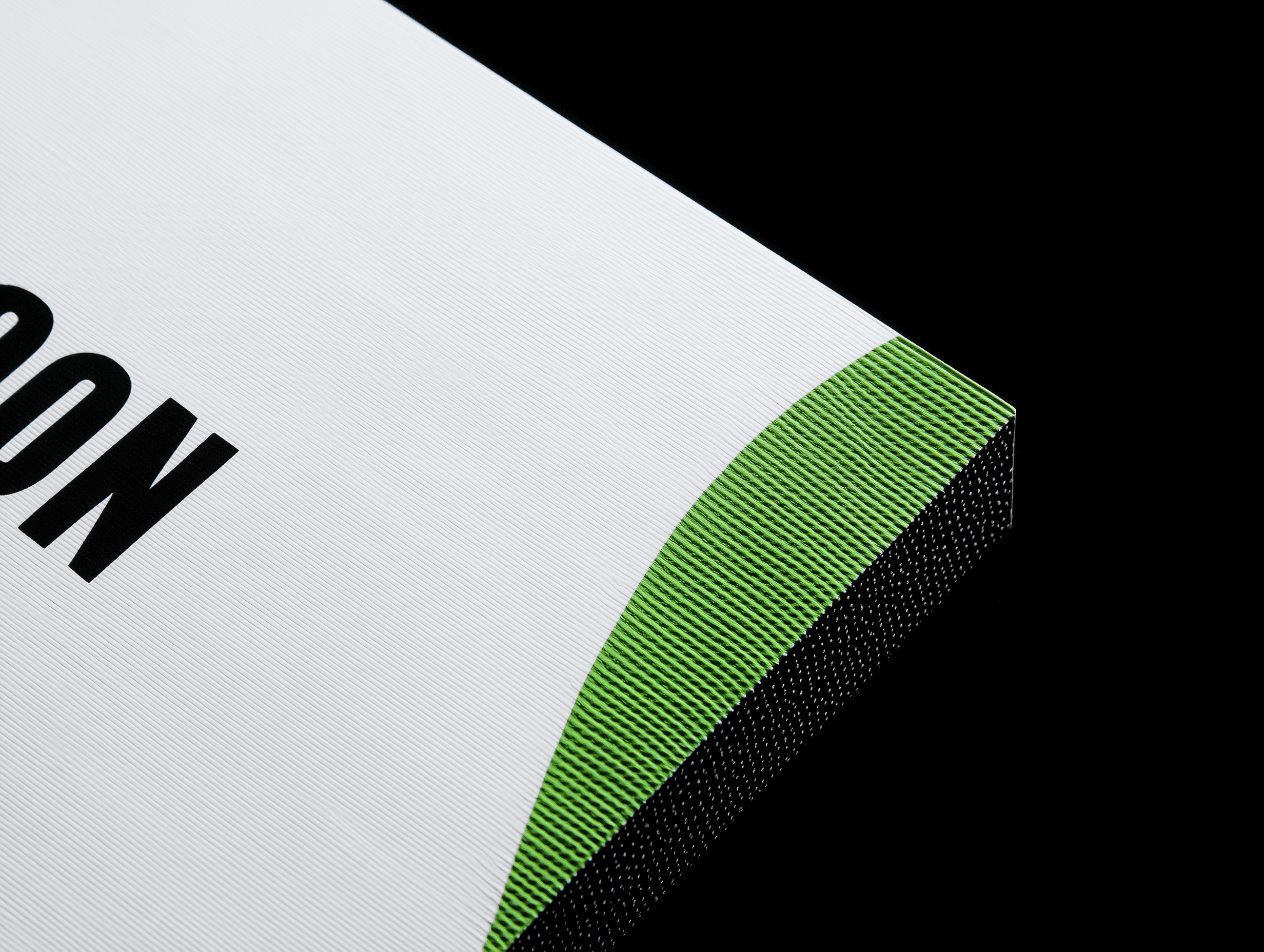 Close-up of minimalist packaging with fine white ribbed texture, a curved green accent, and black typography on a dark background.
