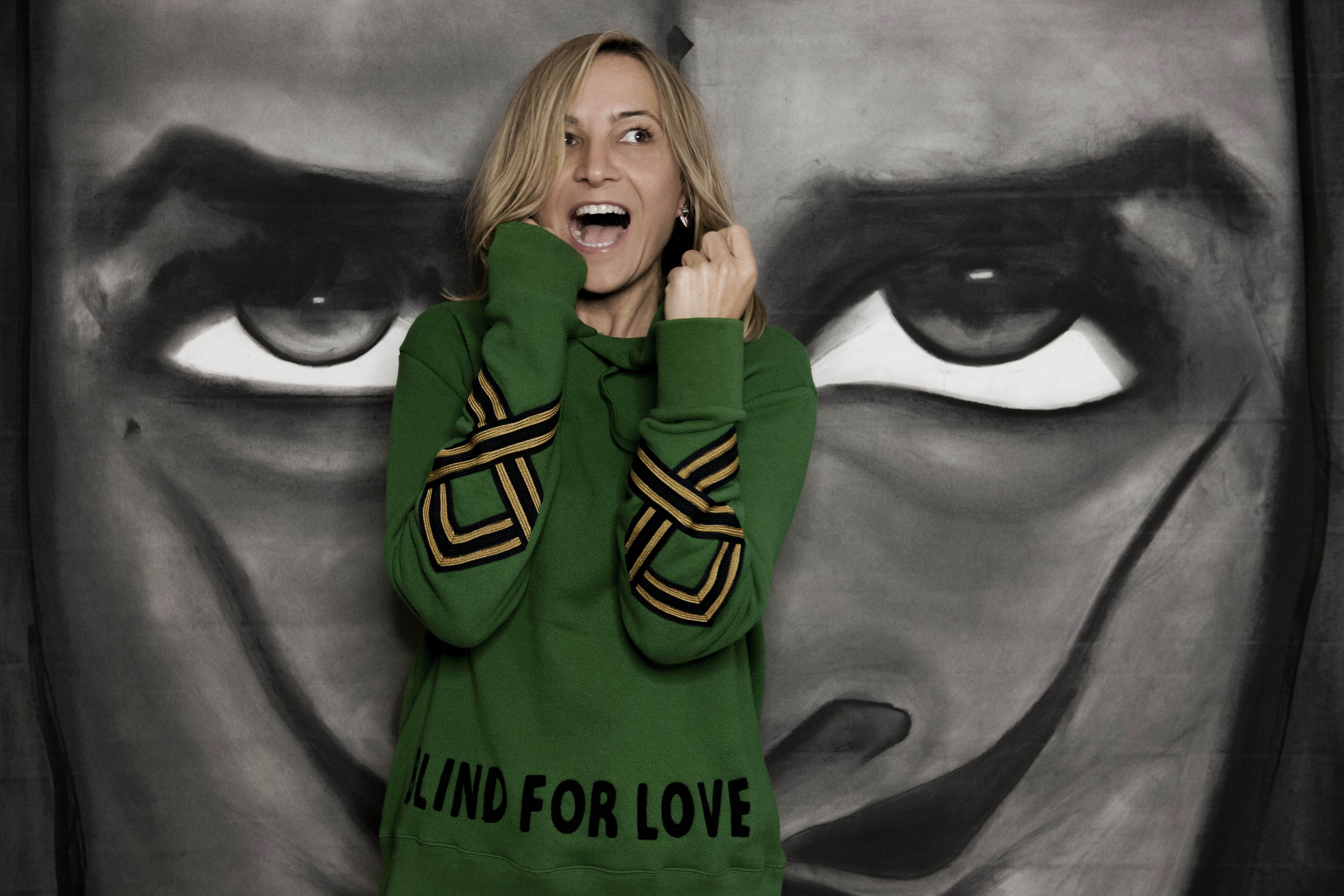 A model dressed in a mustard yellow blazer and cream trousers poses confidently against a minimalist background with sky blue and beige tones, exuding a modern and chic fashion aesthetic.