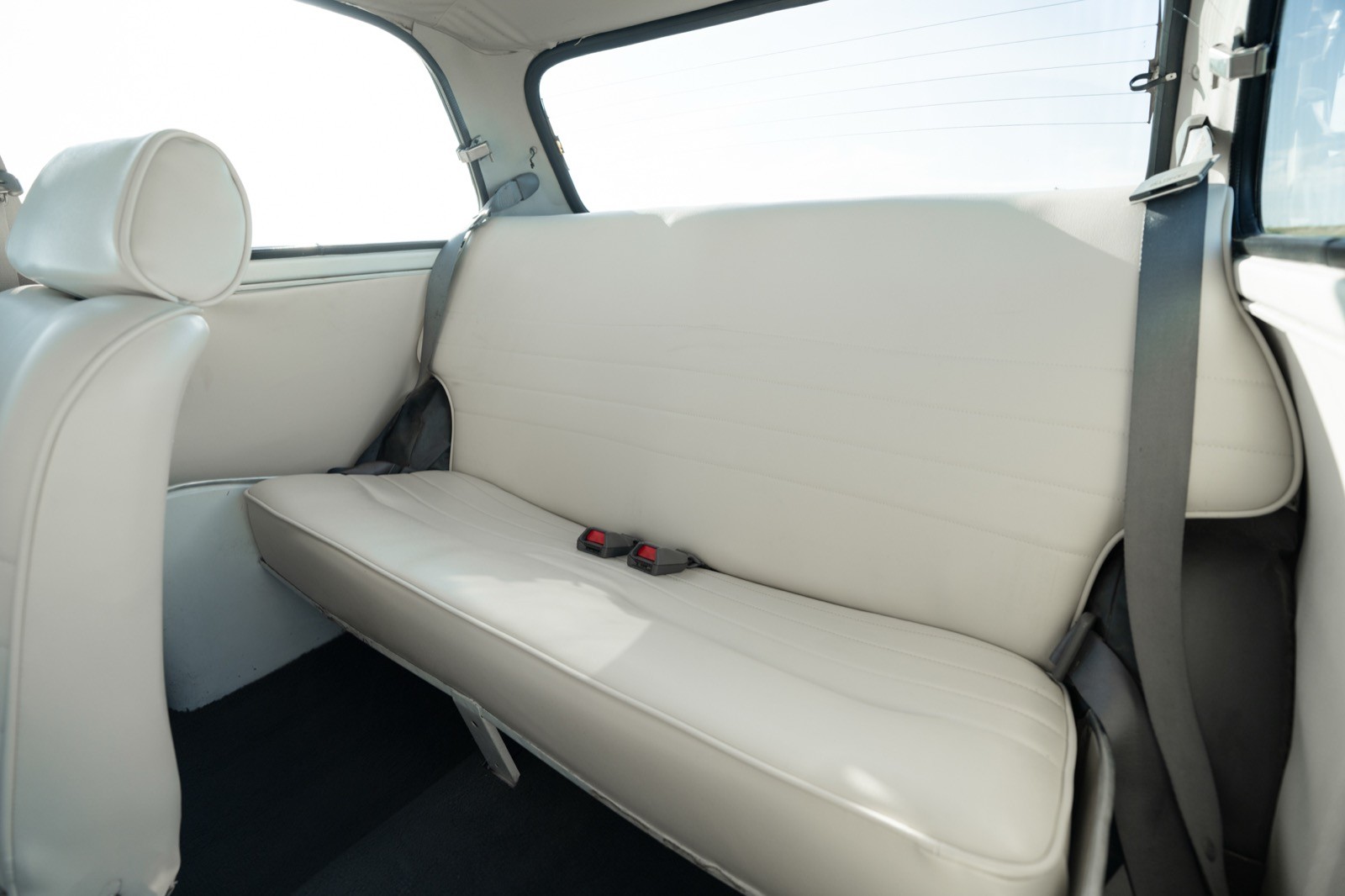 Interior view of a vehicle's rear seat with a simple, modern design in light upholstery.