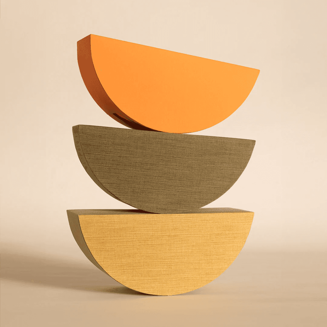 Three textured, semi-circular wooden blocks in orange, olive green, and beige are stacked symmetrically on top of each other against a neutral background, showcasing minimalist design and balance.