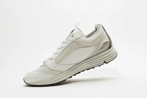 A sleek, modern white athletic sneaker with a lightweight design, featuring subtle gray accents and a textured sole for enhanced grip, photographed against a simple white background.