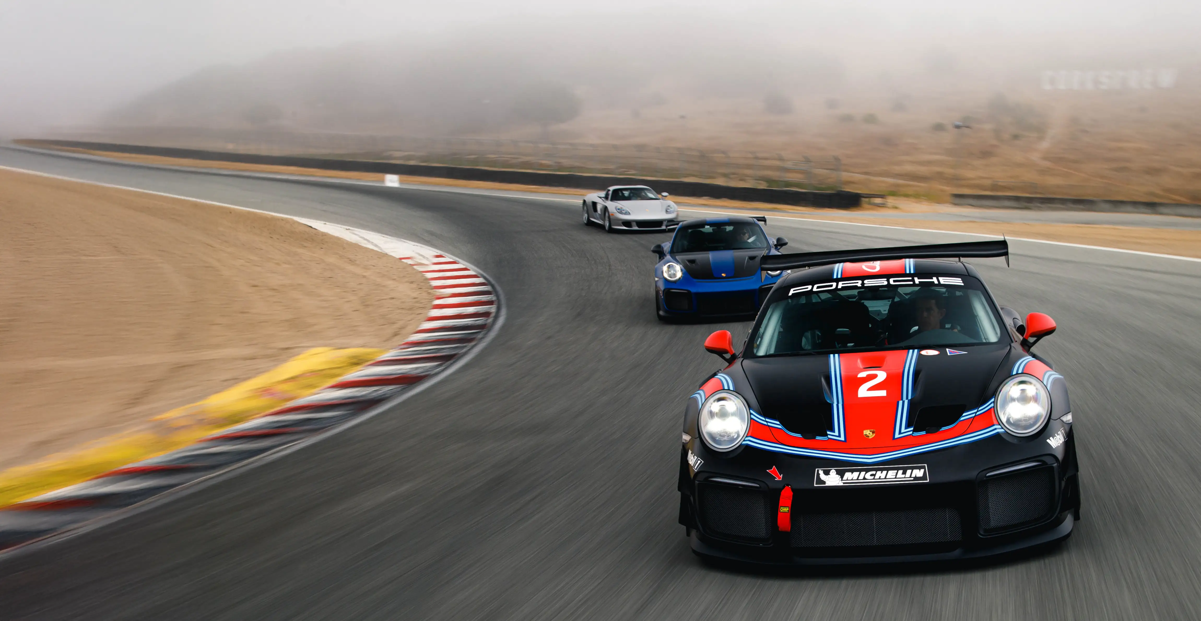 Three Porsche race cars rounding a turn on the track.