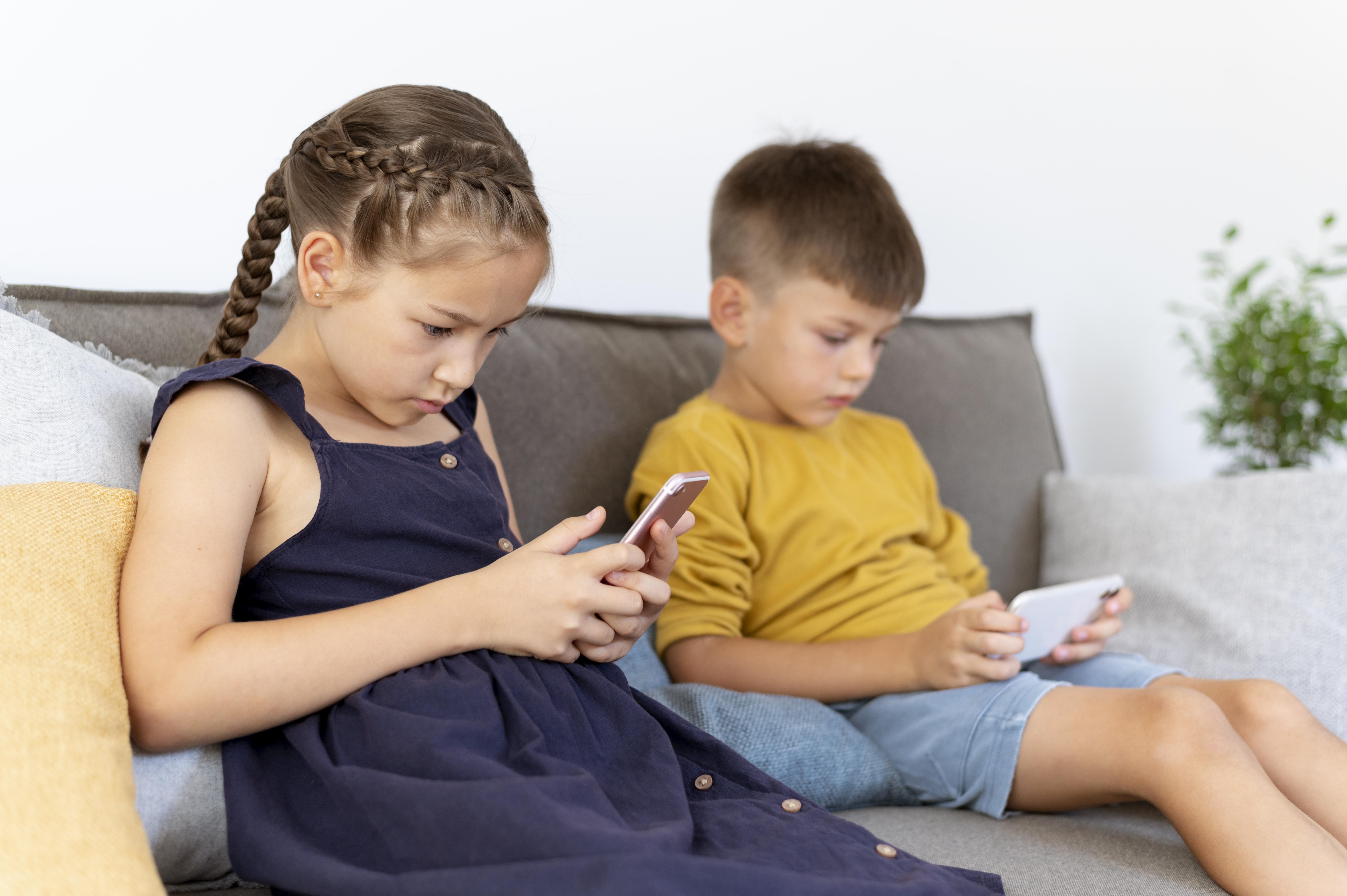 Two children sitting on a sofa with their mobile phone