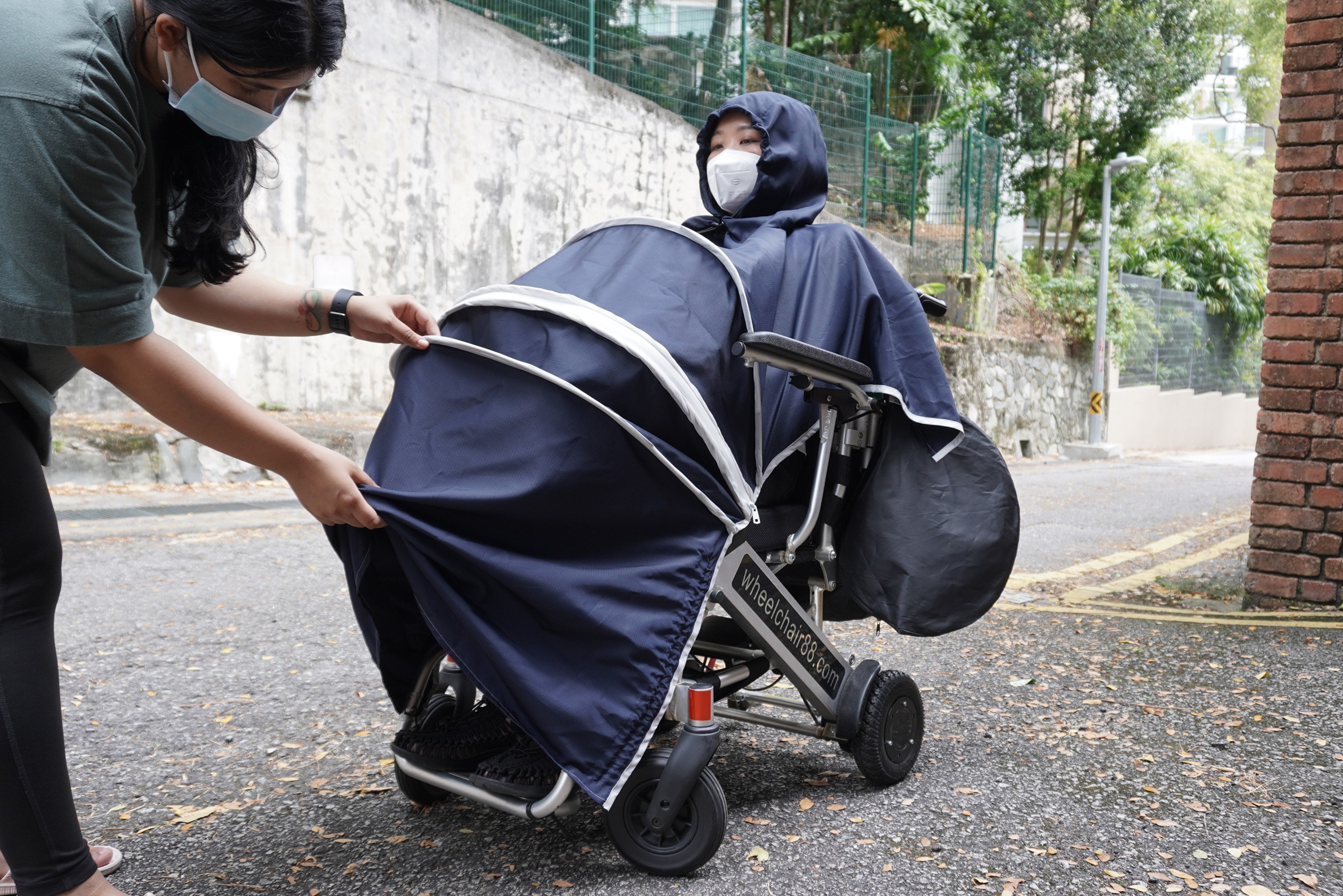 A caregiver helping a wheelchair user put on the wheelchair poncho.