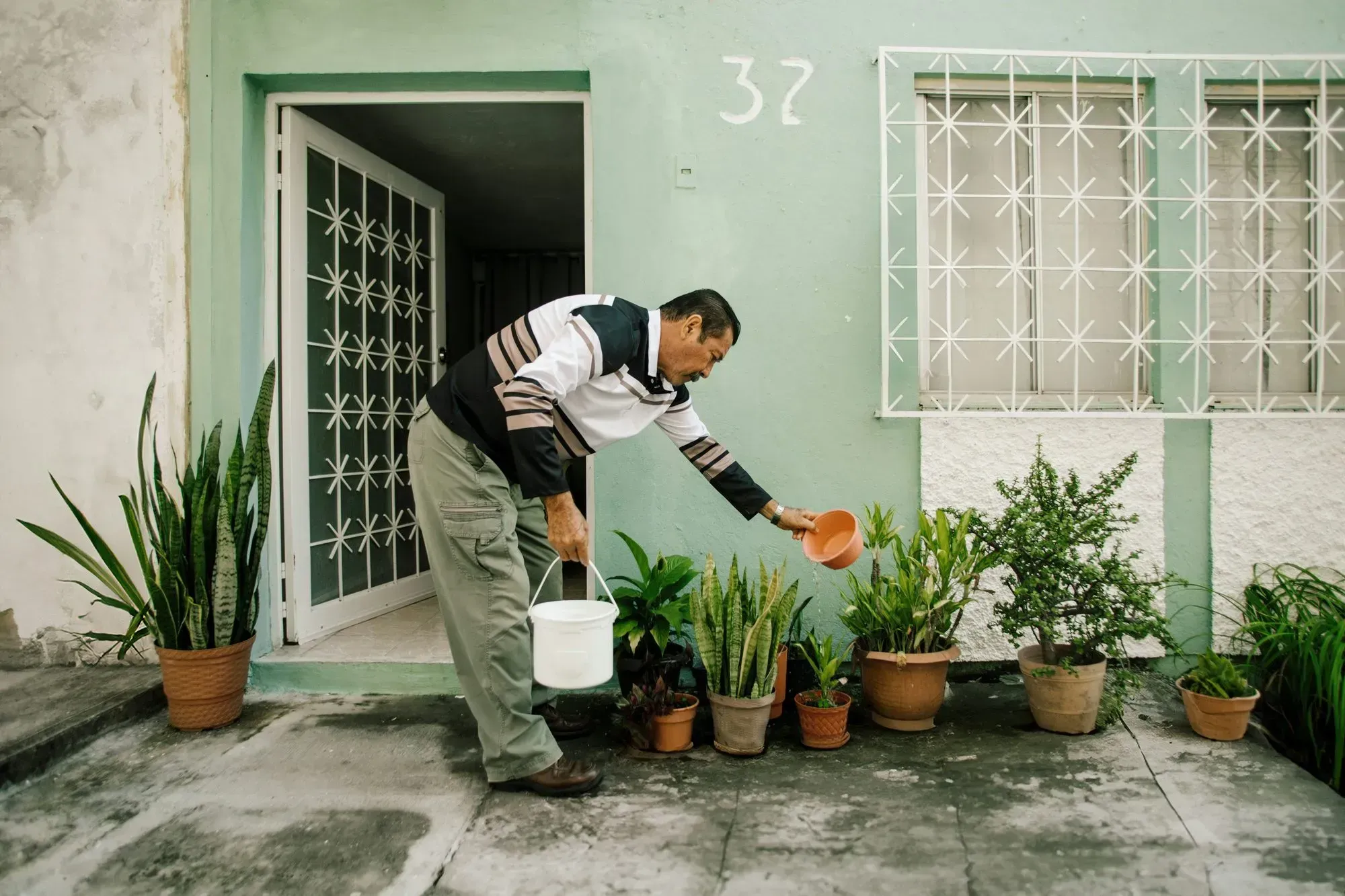 Man watering potted plants outside his home.