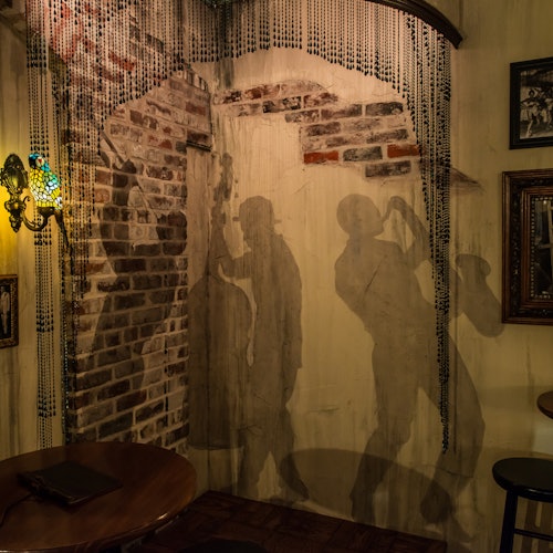 一个灯光昏暗的房间，砖墙上有爵士音乐家的剪影壁画，装饰着珠帘和复古装饰。