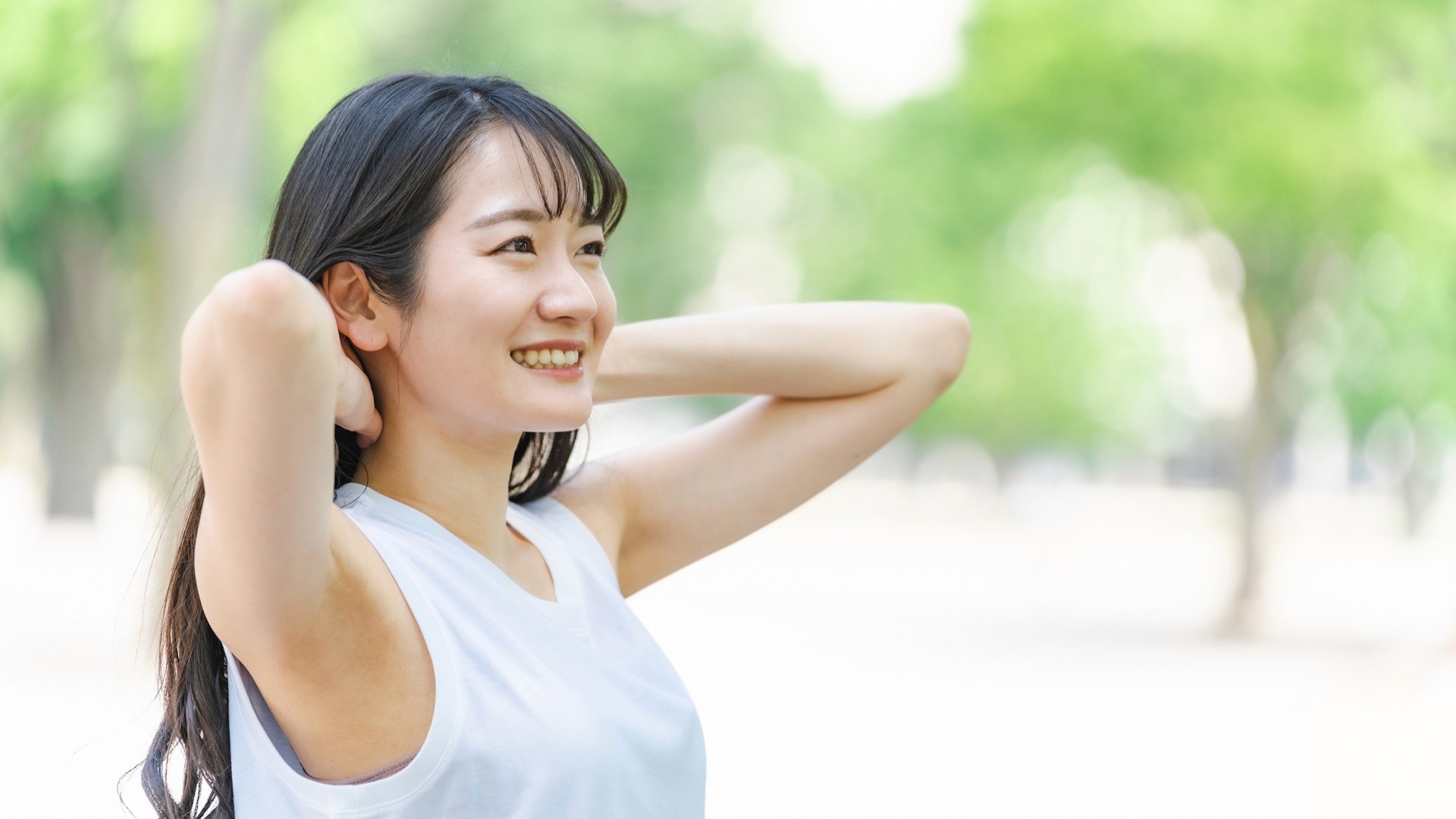 新緑の中で髪を触る笑顔の日本人女性