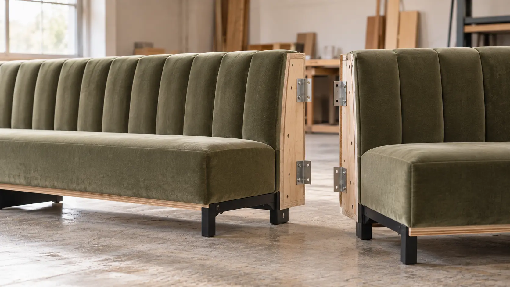 Two sections of a moss velvet channel-tufted banquette on the workshop floor, ready to be joined