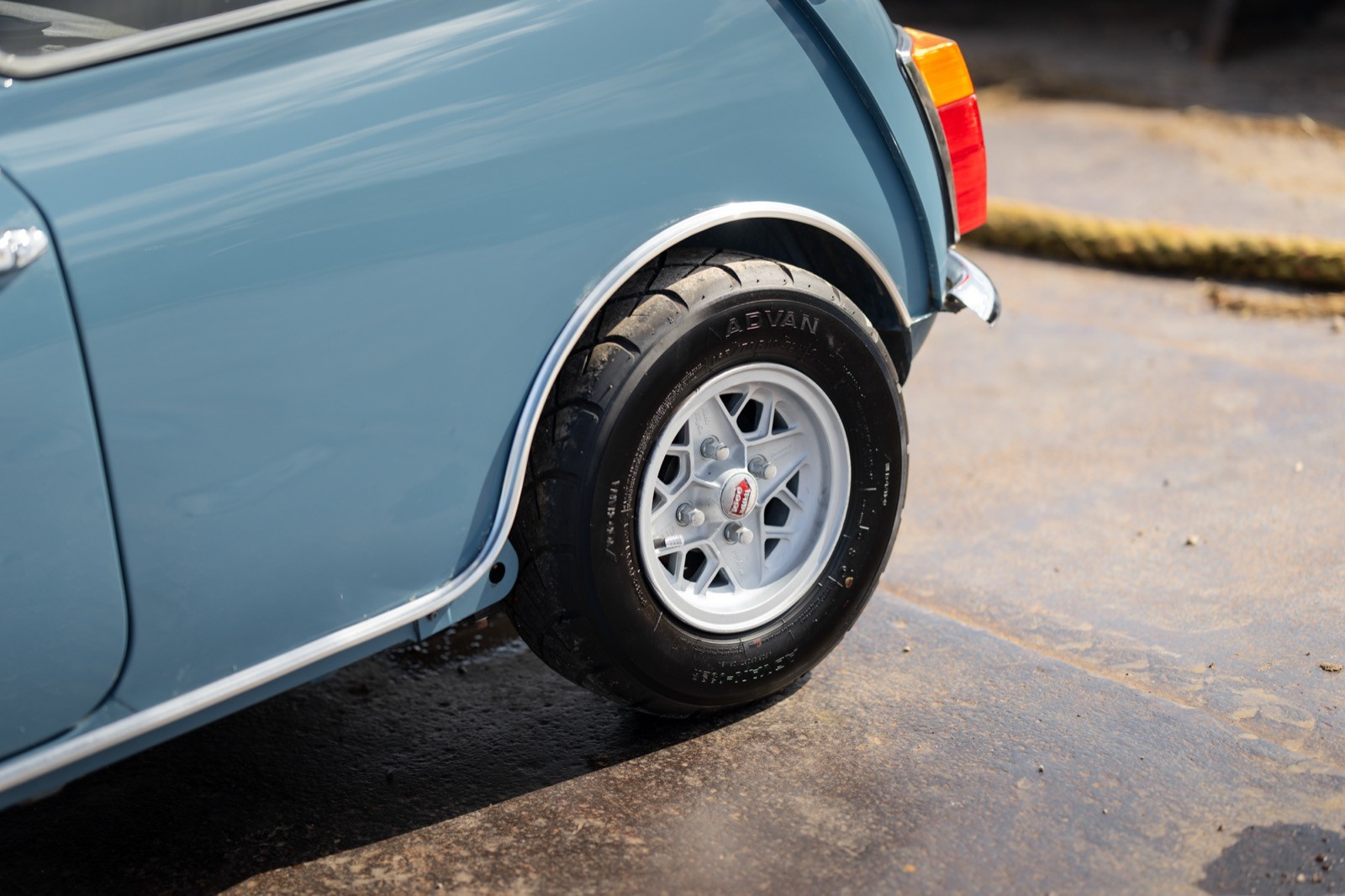 Close-up of a light blue car's rear wheel and fender, showing sleek lines and polished chrome details.