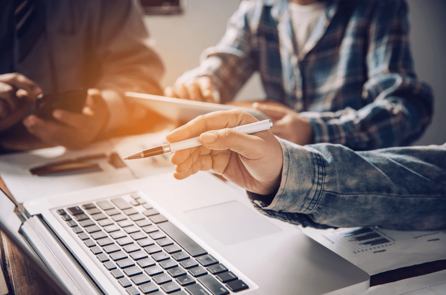 Close-up of team members collaborating over a laptop with data sheets, representing how uncoordinated Amazon PPC portfolios can cause hidden keyword overlap and wasted ad spend without unified campaign visibility.