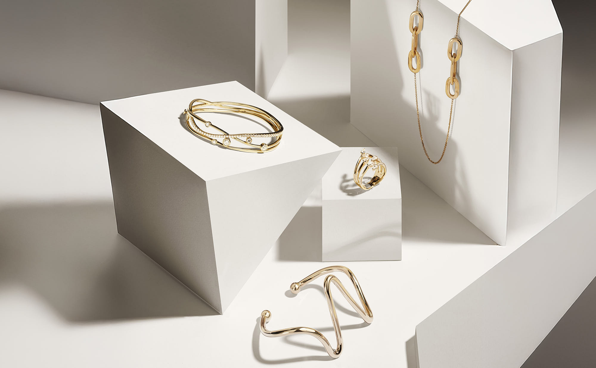 A collection of elegant jewelry displayed on minimalist white pedestals, including rings and bracelets.