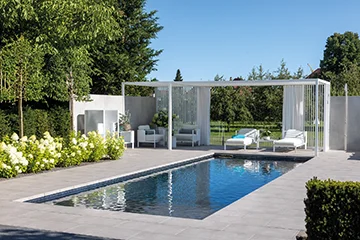 Rechteckpool mit weißer Pergola, weißen Loungemöbeln und Blütensträuchern