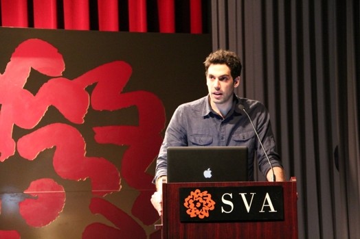 a man giving a speech from a stand in the "designer as" thesis presentation