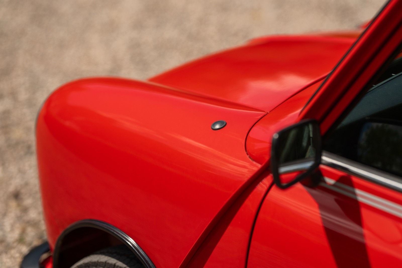 Close-up of a glossy red car's hood, showcasing its smooth finish and corner detail.