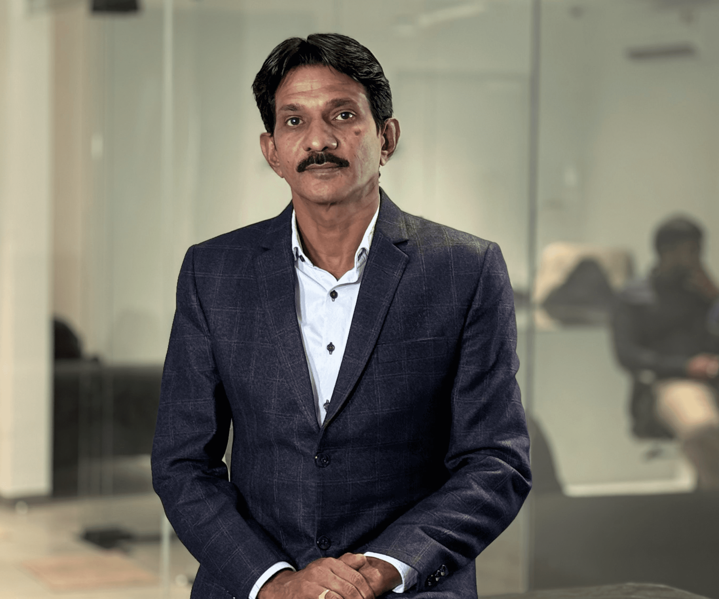 Young man with wavy hair wears a dark overcoat, rust-colored sweater, white shirt, and patterned tie, exuding a poised and sophisticated demeanor.