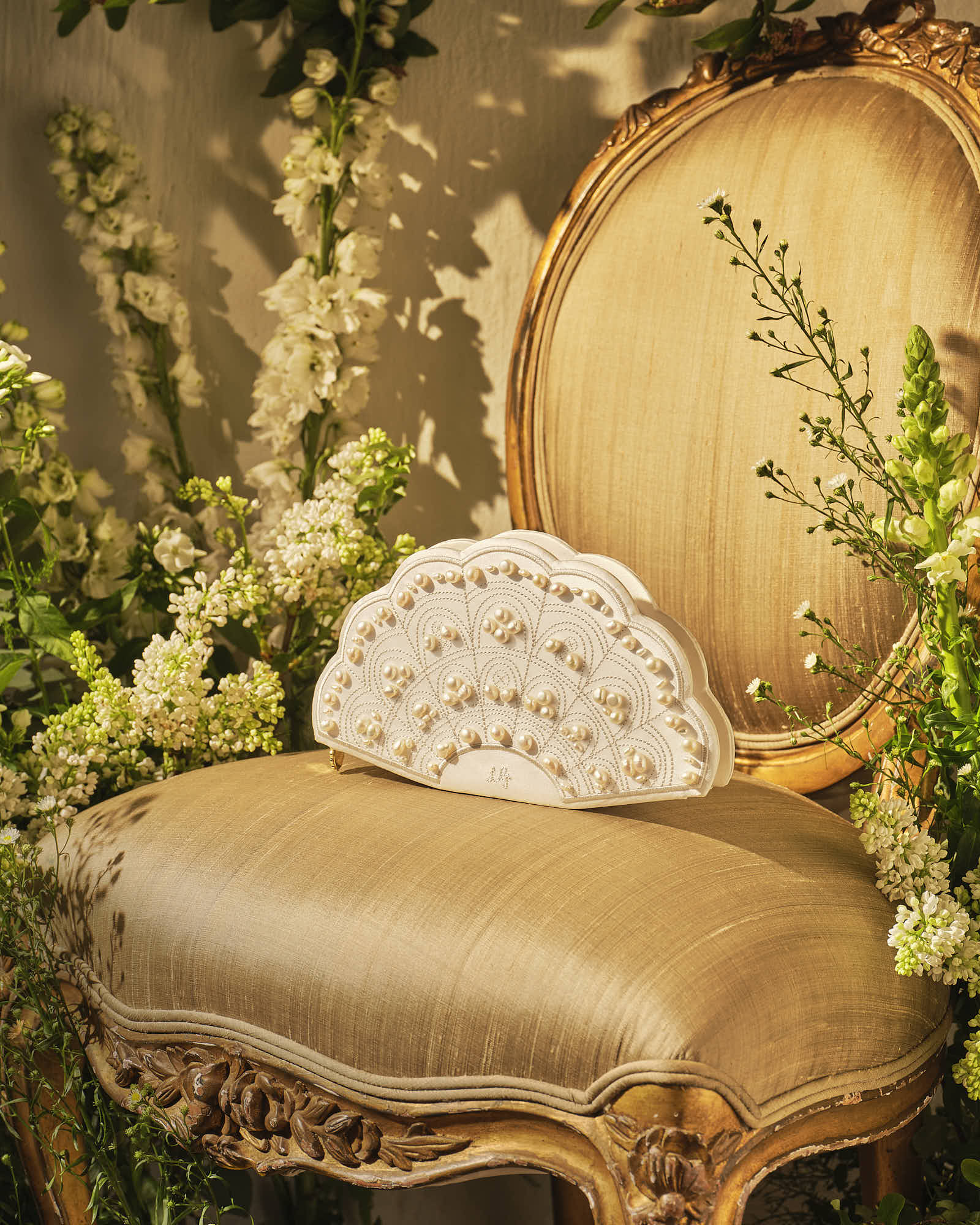 Elegant white clutch on ornate vintage chair with floral background.