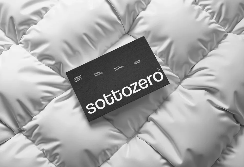 A black rectangular card with bold white typography, placed on a textured white quilted fabric. The contrast between the sleek card and the soft, padded background creates a modern and sophisticated look.