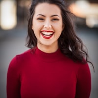 A smiling woman with long dark hair wearing a red turtleneck sweater.