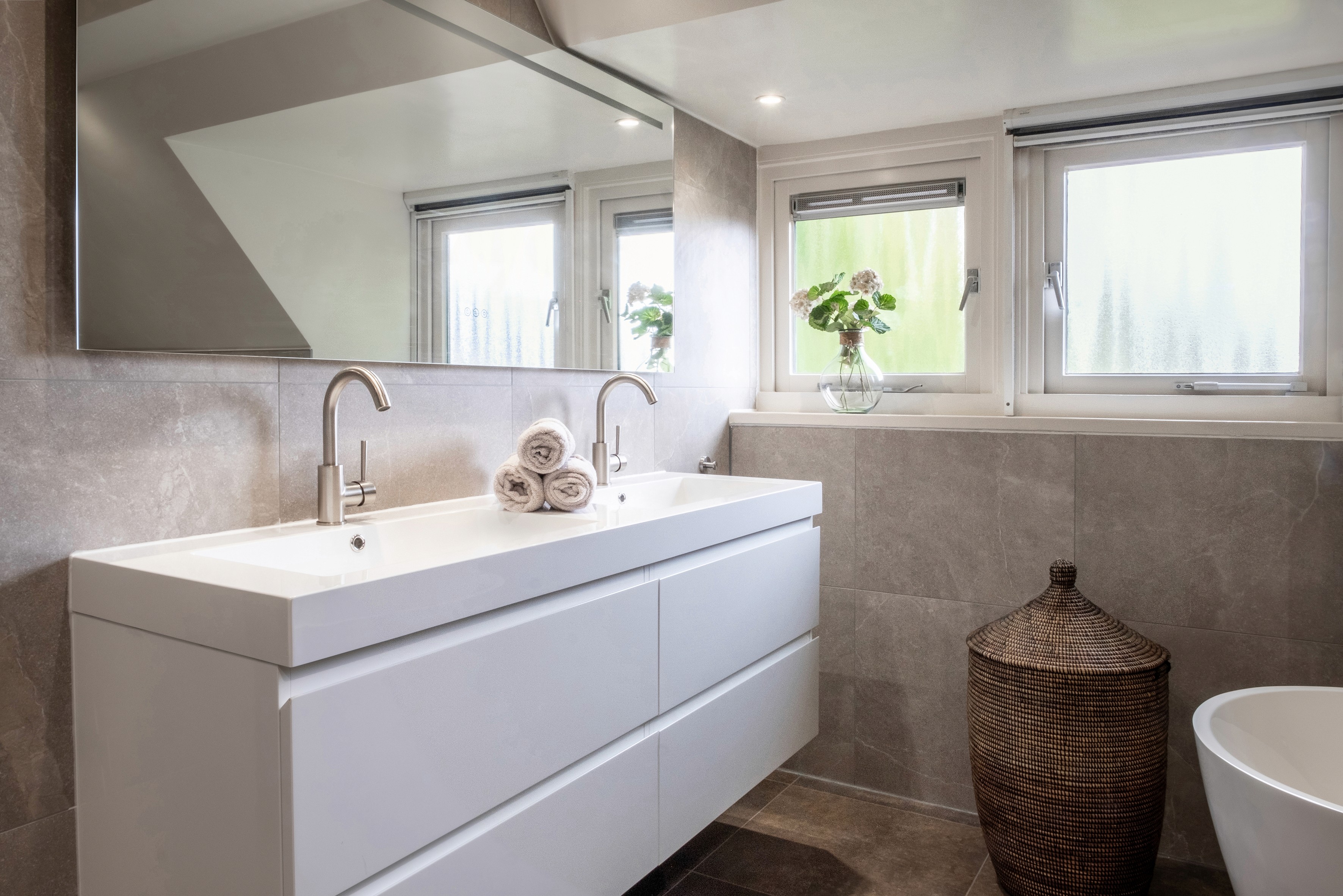 Moderne wastafel met ronde spiegel en marmeren achterwand – exclusieve badkamerrenovatie in hotelstijl.