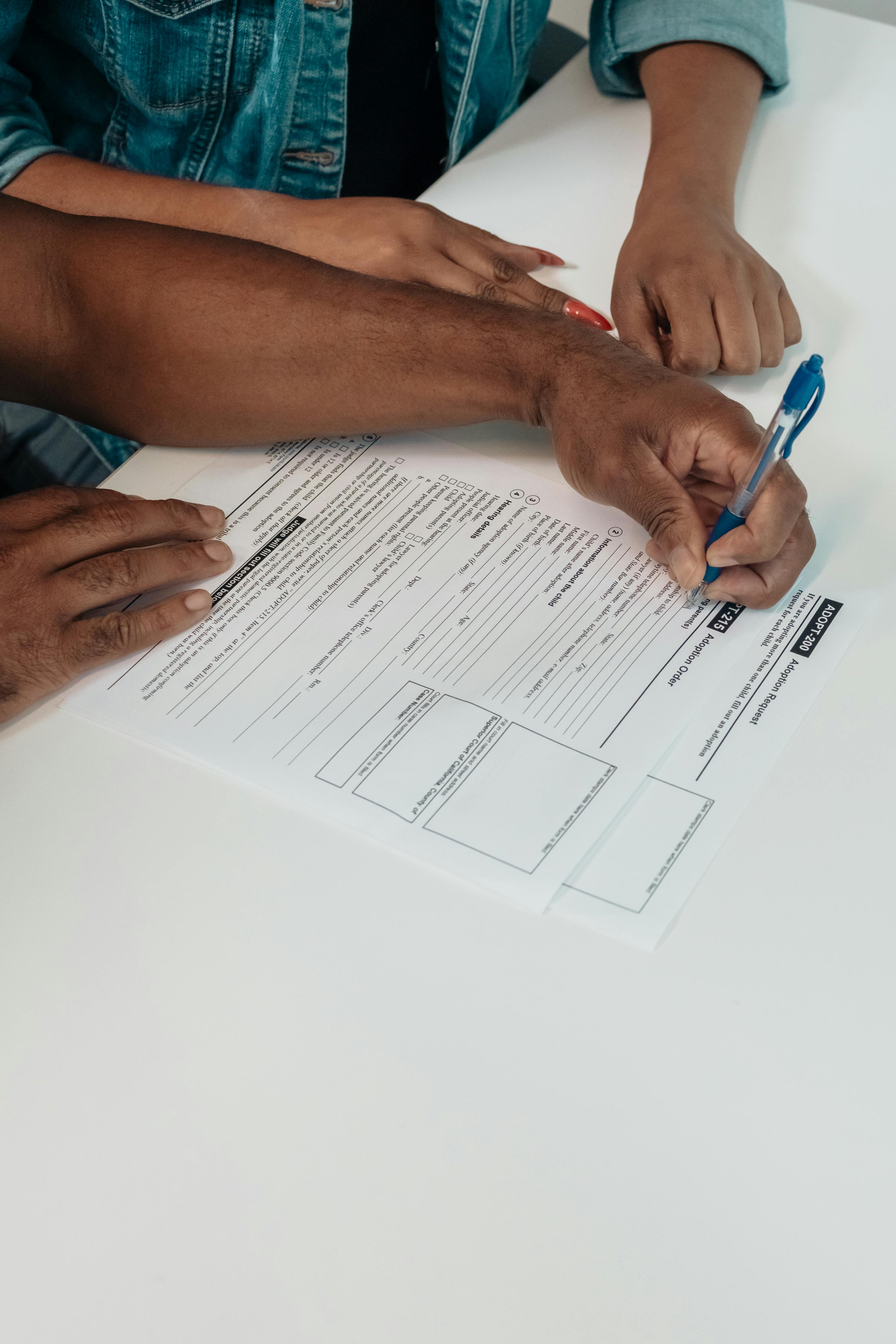 A small model house with a red facade and grey roof sits on a wooden table next to a silver keychain holding two keys, symbolizing real estate and home ownership.