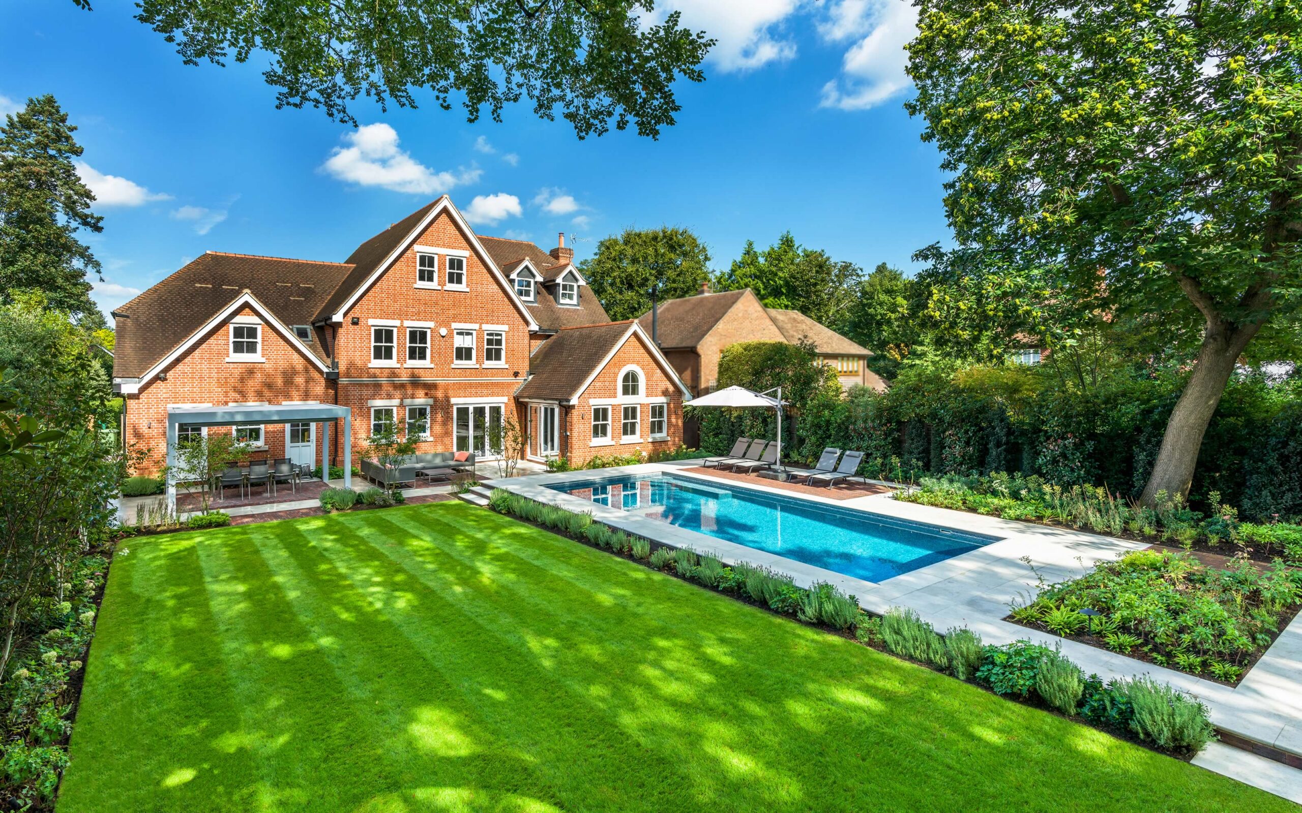 A beautiful backyard featuring a green lawn, modern home, and a swimming pool under a clear blue sky.