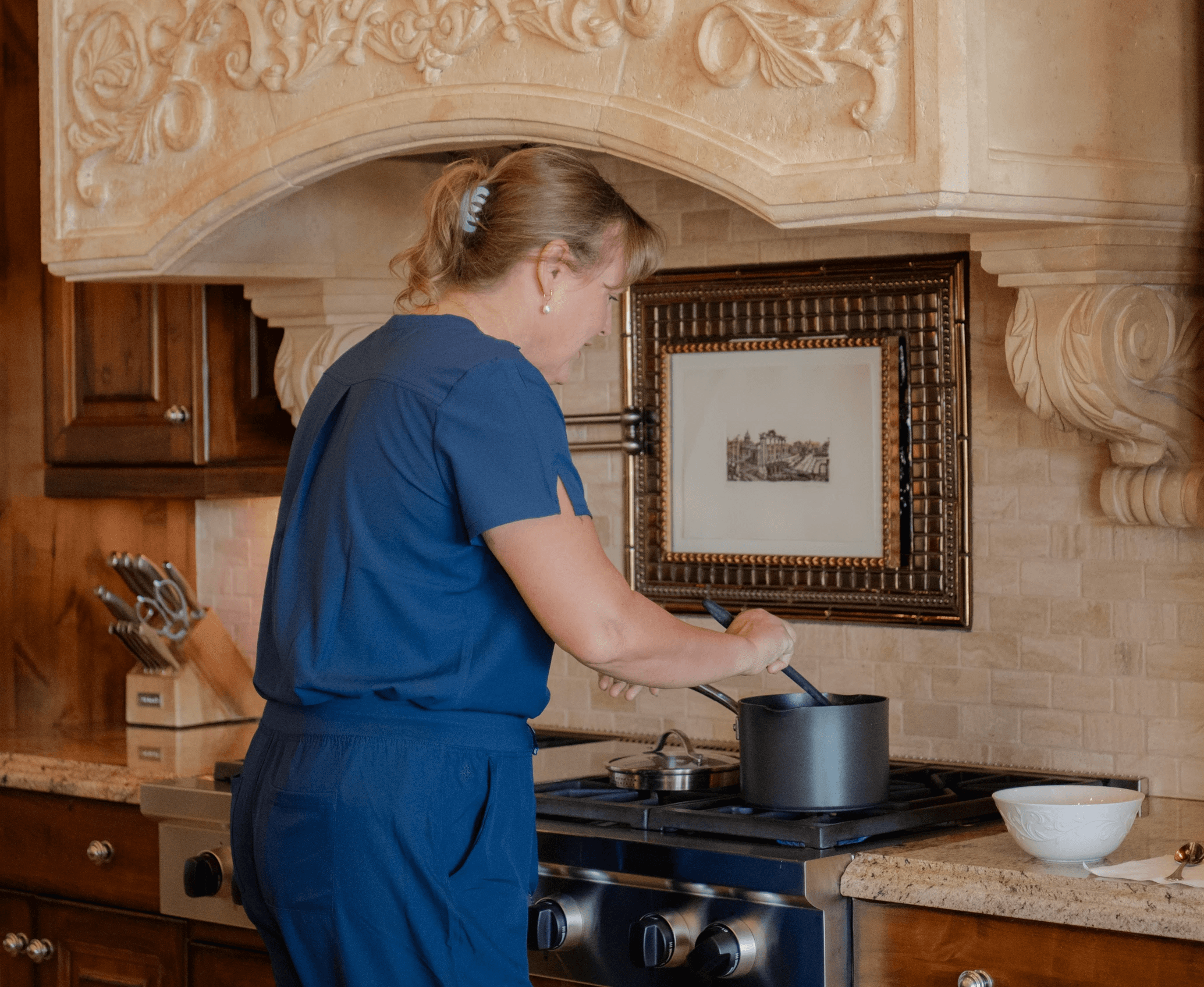 A woman cooks on a stove in a kitchen with ornate decorations.