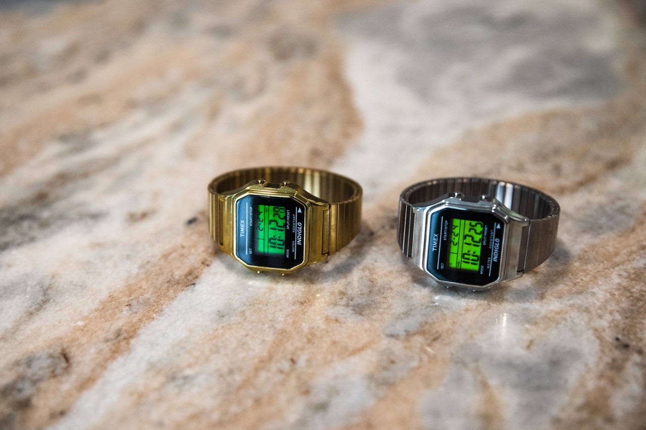 Two metal digital wristwatches on a marble countertop, shown side by side.