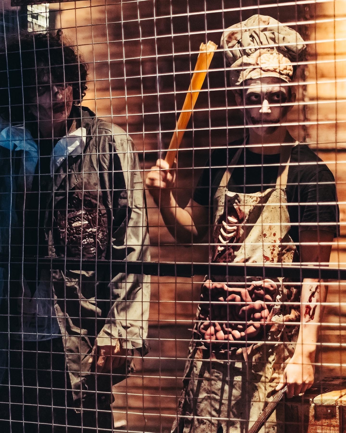 Zombie butcher scare actors behind metal cage with blood stained costumes and horror makeup for Halloween event in Dubai