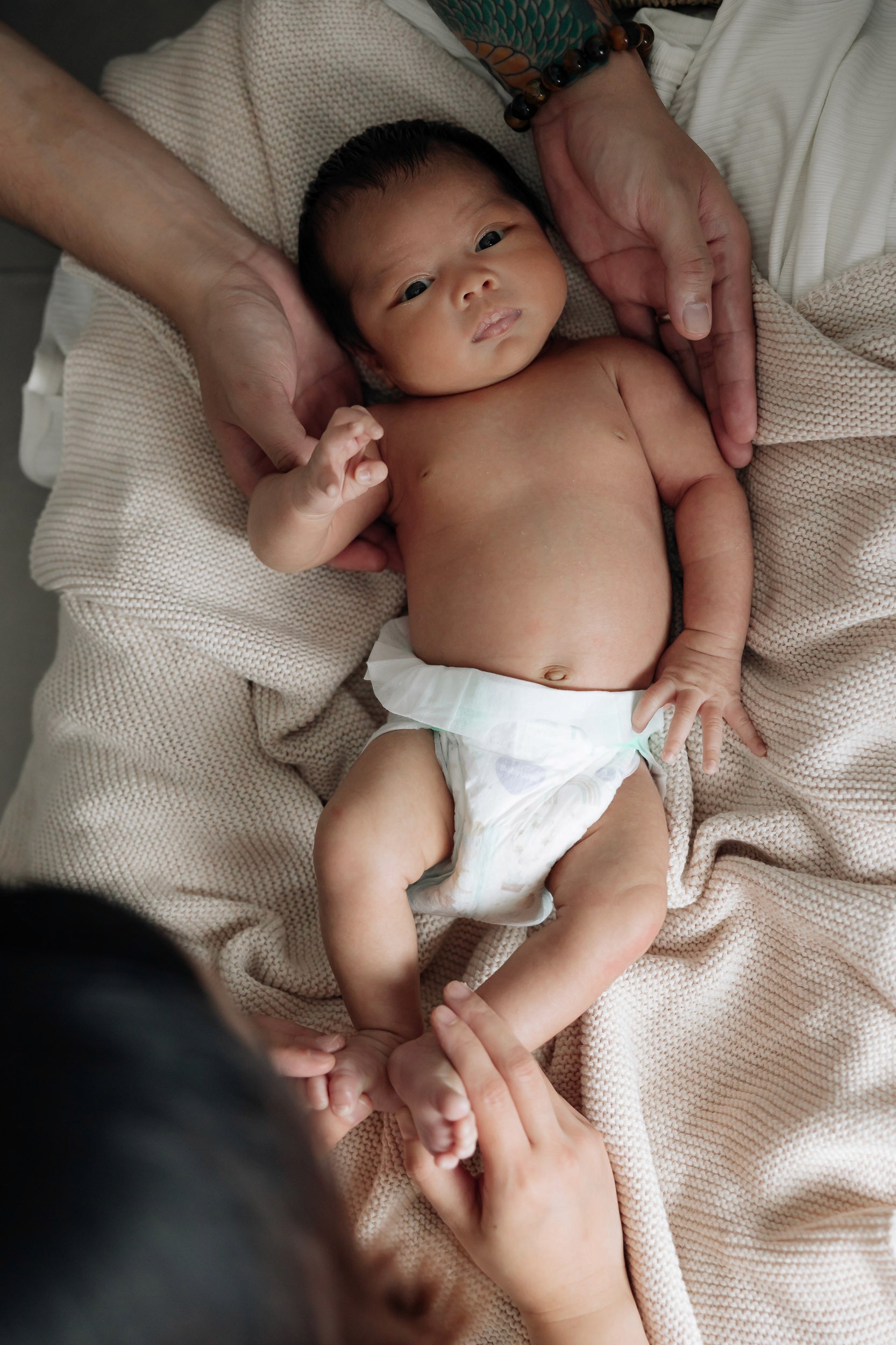 Baby laying down with parents hands comforting