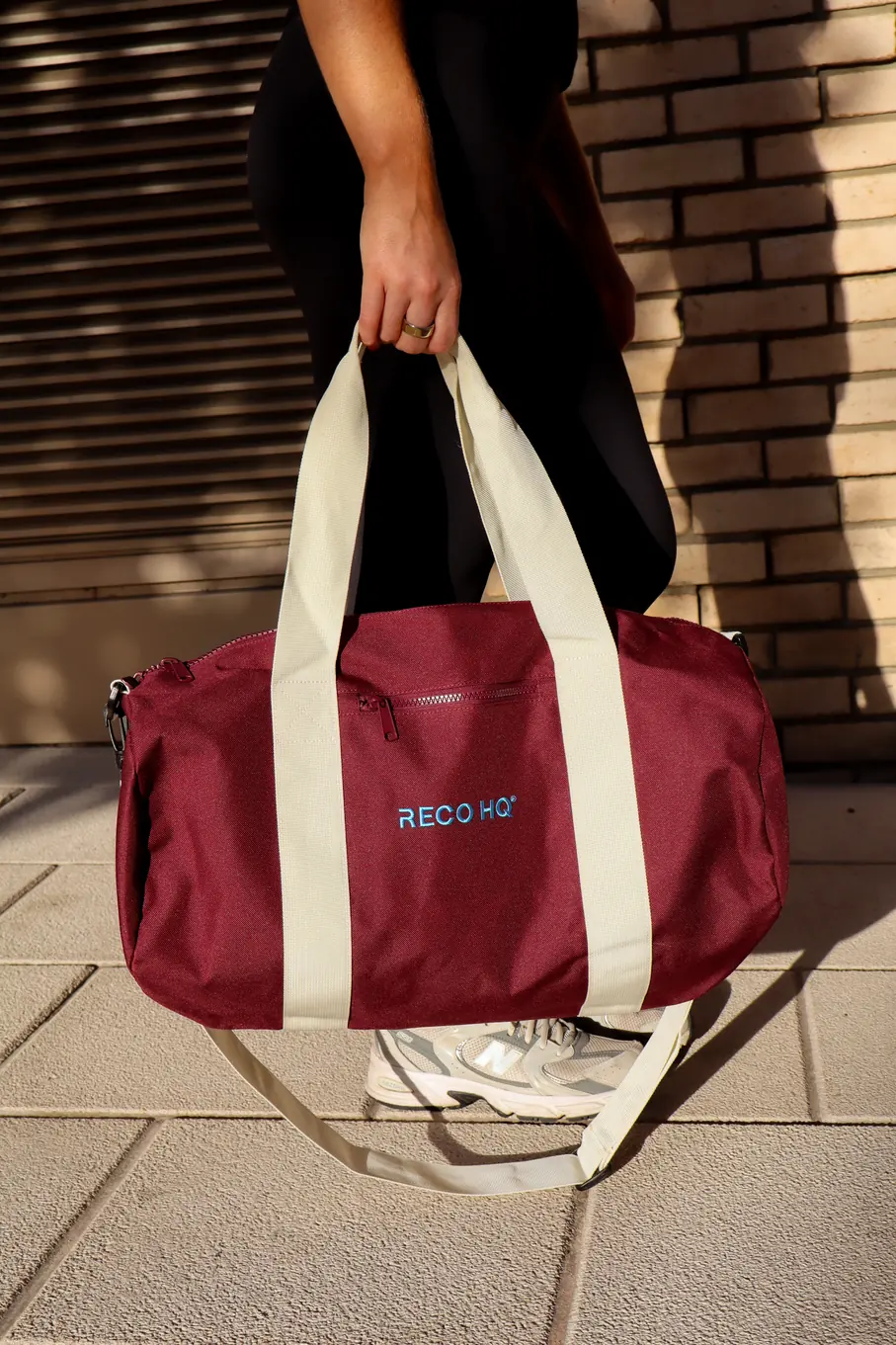 Burgundy RECO HQ duffel bag with cream straps, carried by the handles