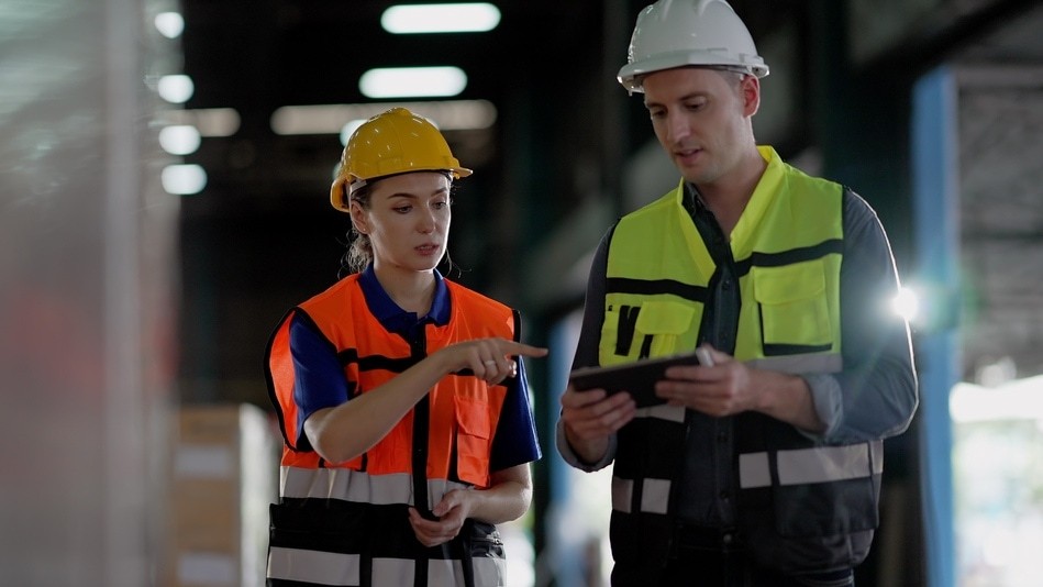 Supervisores con chaleco y casco revisando protocolo de seguridad en bodega industrial