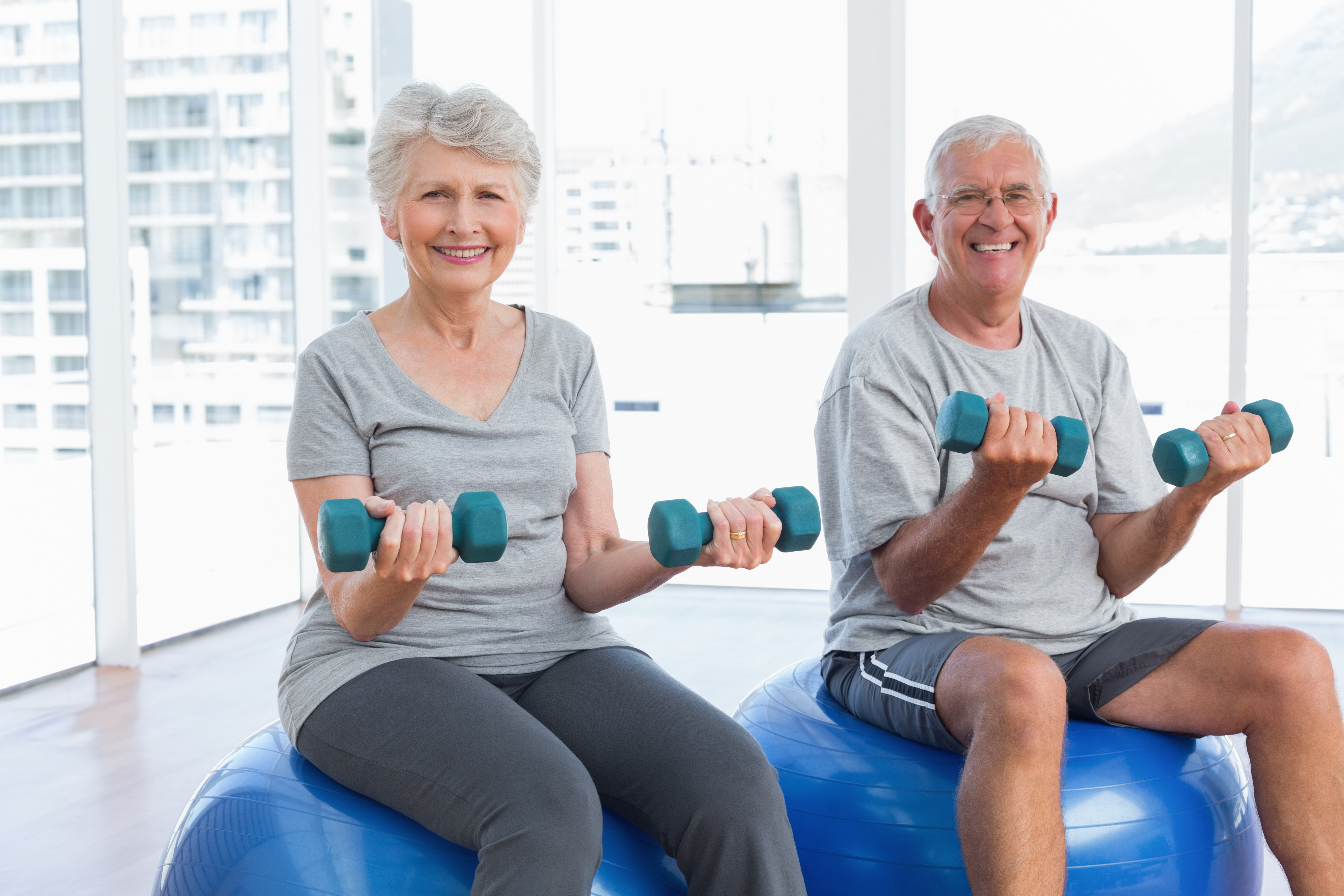 an elderly woman and man sitting on balance balls while holding hand weights