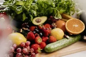 A variety of fresh fruits and vegetables arranged on a wooden surface, including grapes, oranges, and cucumbers.