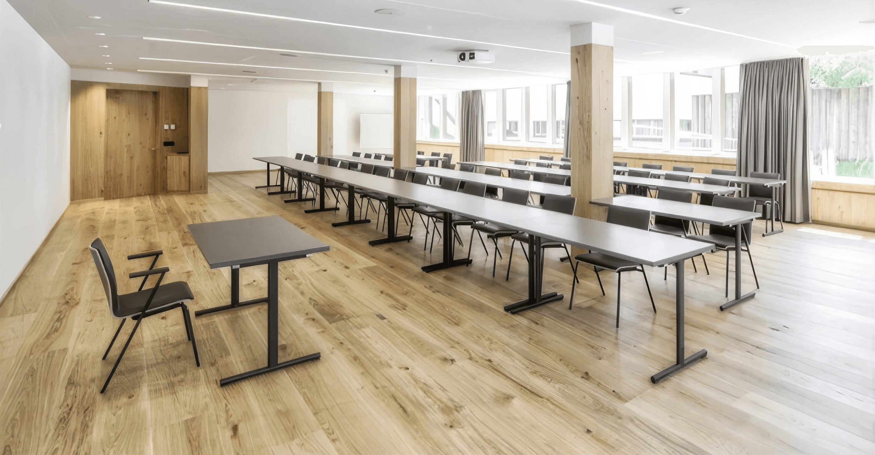 MW Interior  - Heller Seminarraum im Sporthotel Montafon mit anthrazitfarbenen Seminar­tischen in Reihenbestuhlung, schwarzen Stühlen, Massivholzparkett und Holzpfeilern" Beschreibung: Großzügiger, flexibler Seminarraum mit anthrazitfarbenen Klapptischen, schlichter Reihenbestuhlung und breitem Massivholzparkett – der Raum verbindet alpine Materialsympathie mit professioneller Tagungsfunktionalität.