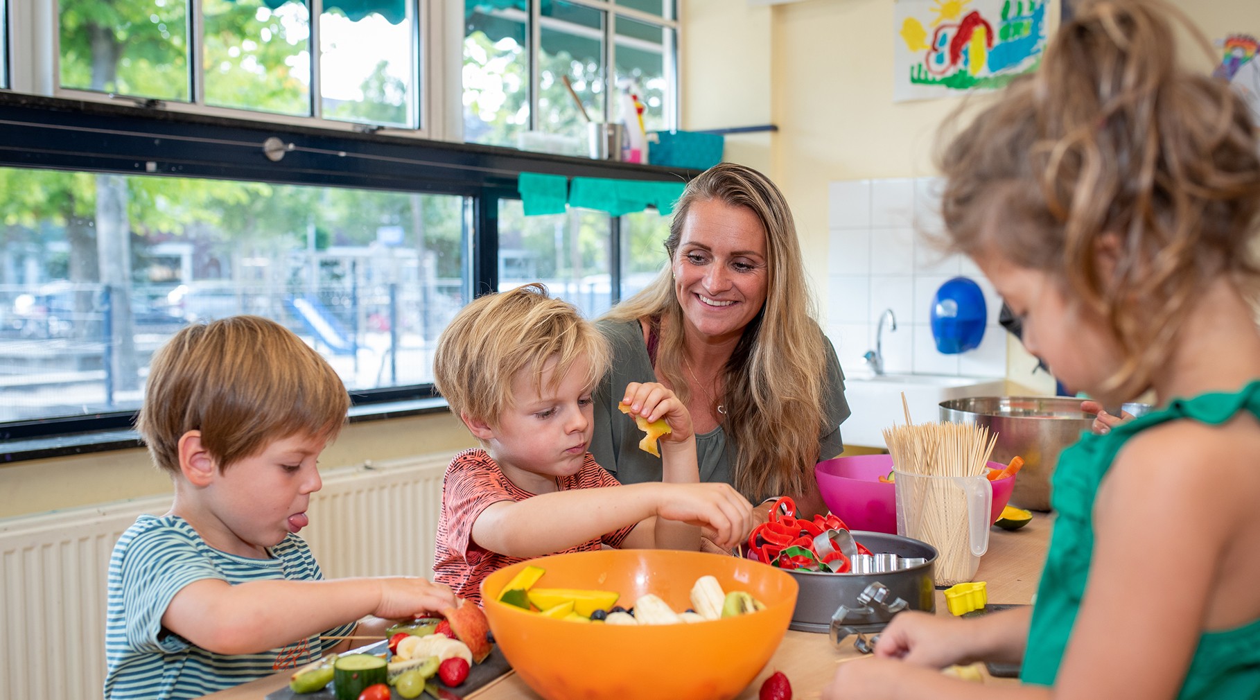 Een jonge jongen met blond haar en een groen T-shirt schommelt lachend op een autoband aan een rood touw in een groene, boomrijke speeltuin.