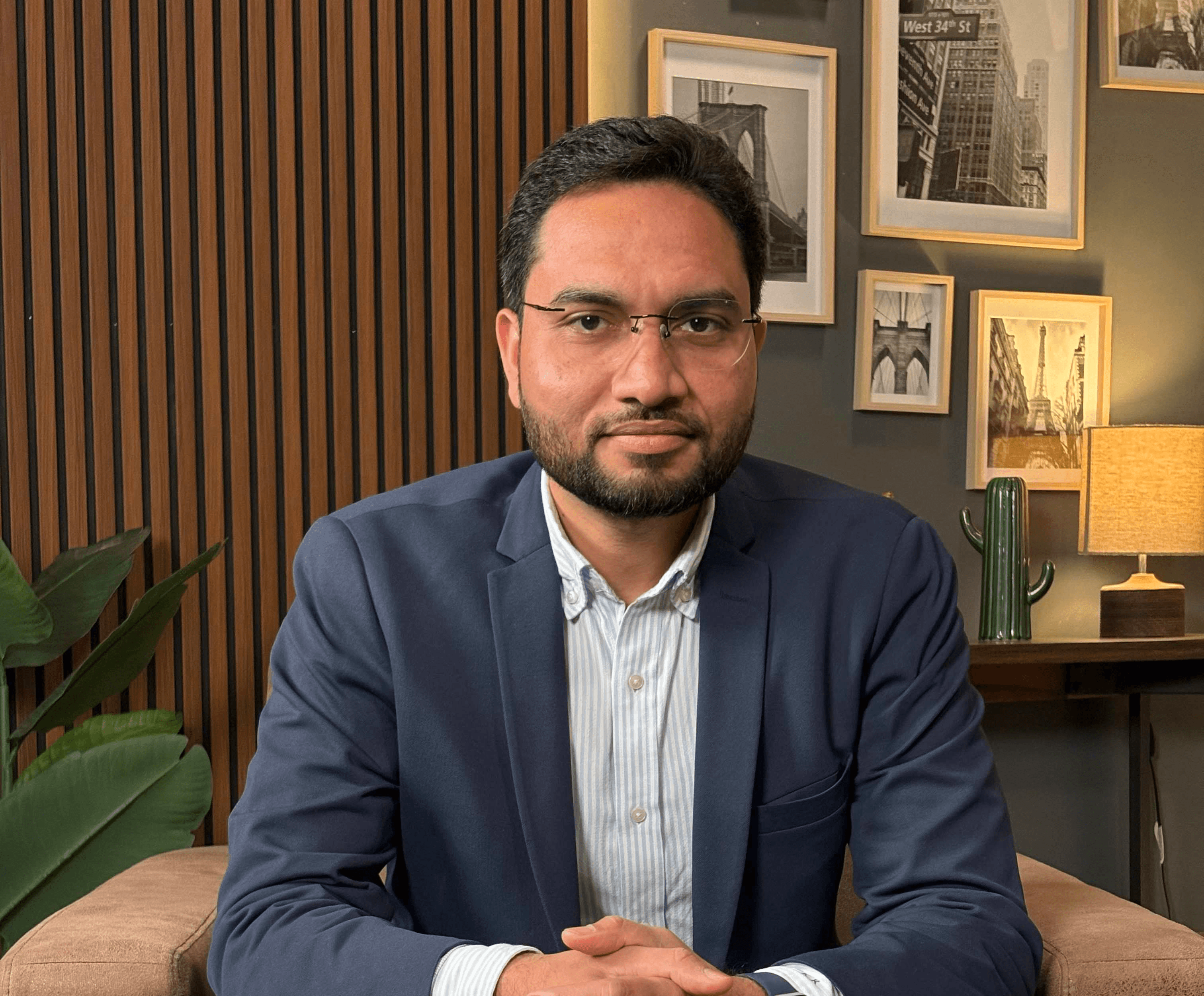 Asian man with glasses in a creative workspace, surrounded by colorful abstract art and stationery on a cluttered desk.