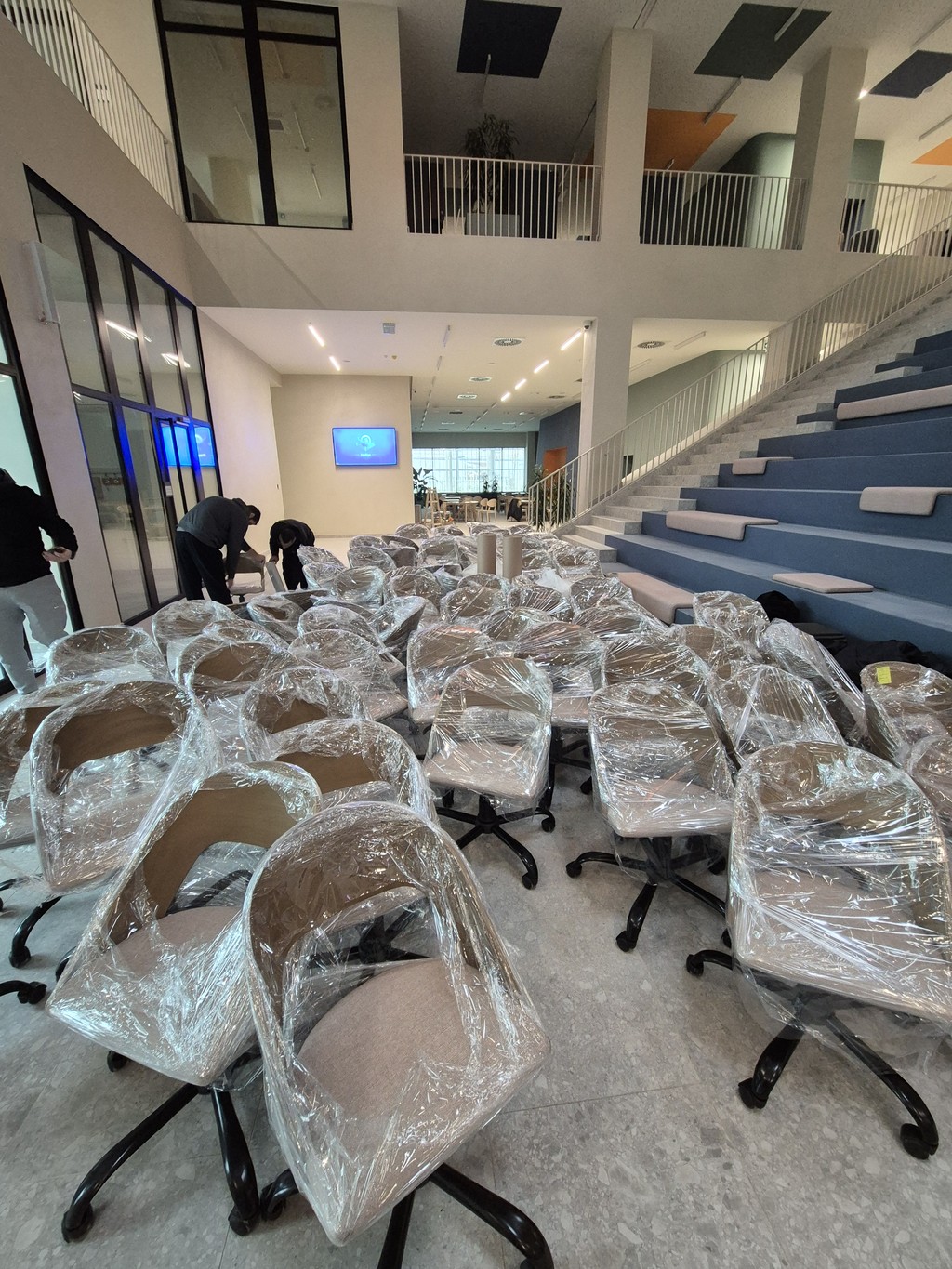 Veliki broj kancelarijskih stolica pažljivo upakovanih u zaštitnu foliju u modernom poslovnom prostoru.